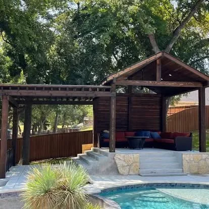 Corrugated metal fence with wooden pavilion and stone patio by pool