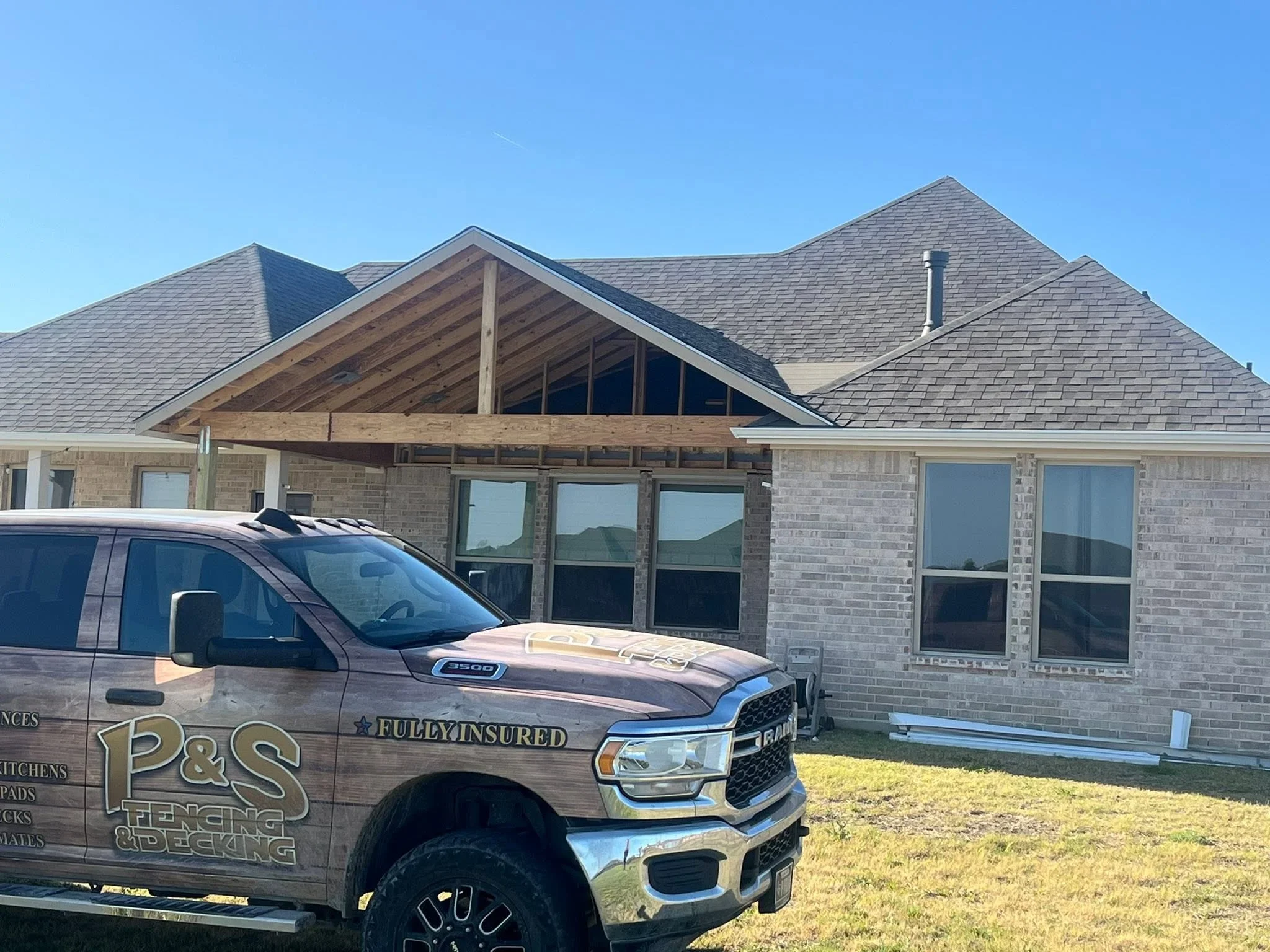 New brick home with gray asphalt shingle roof, timber gable framing, and multi-pane windows under construction