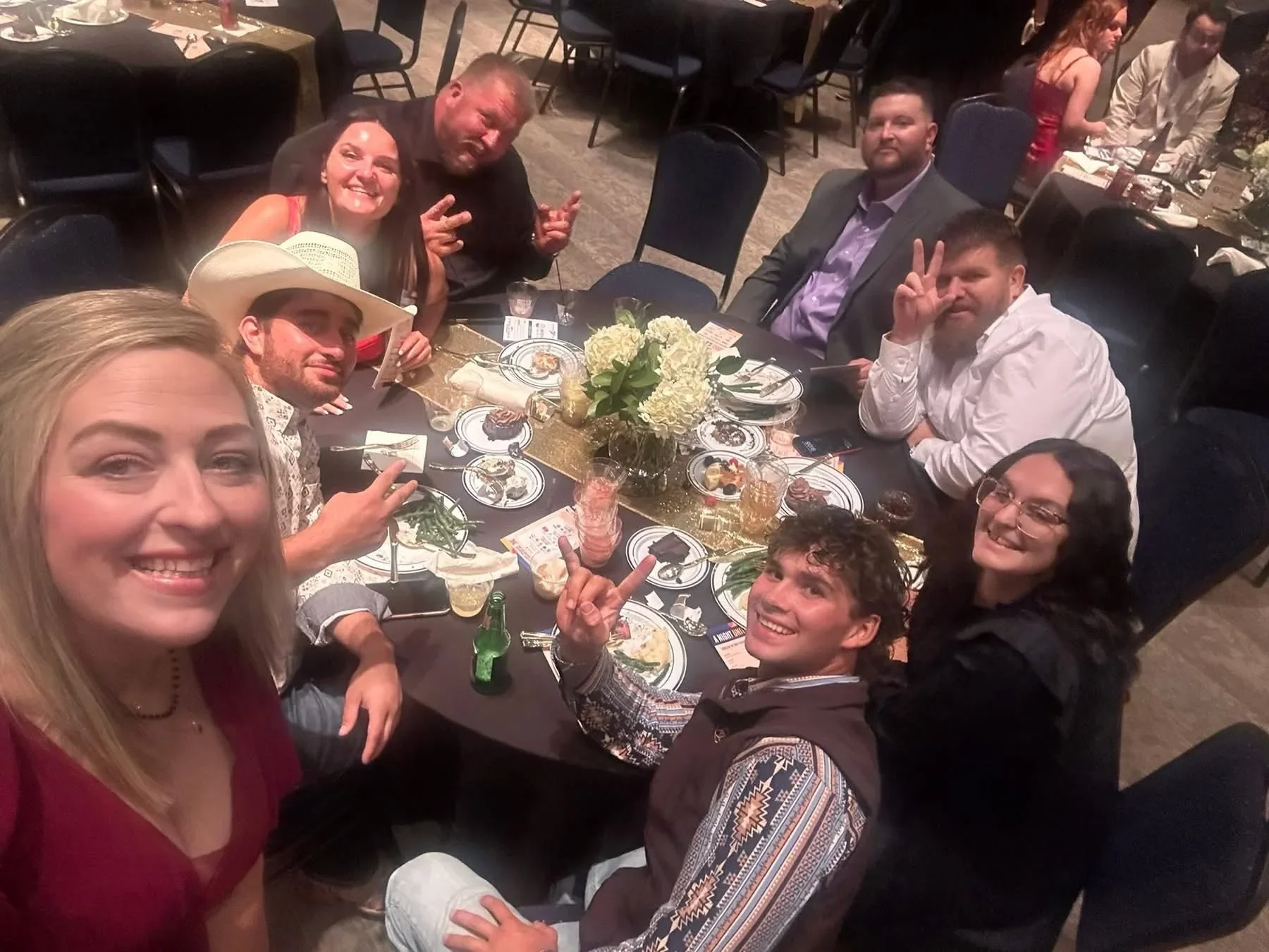 Formal dining event with round tables, white floral centerpieces, place settings, and guests in business attire
