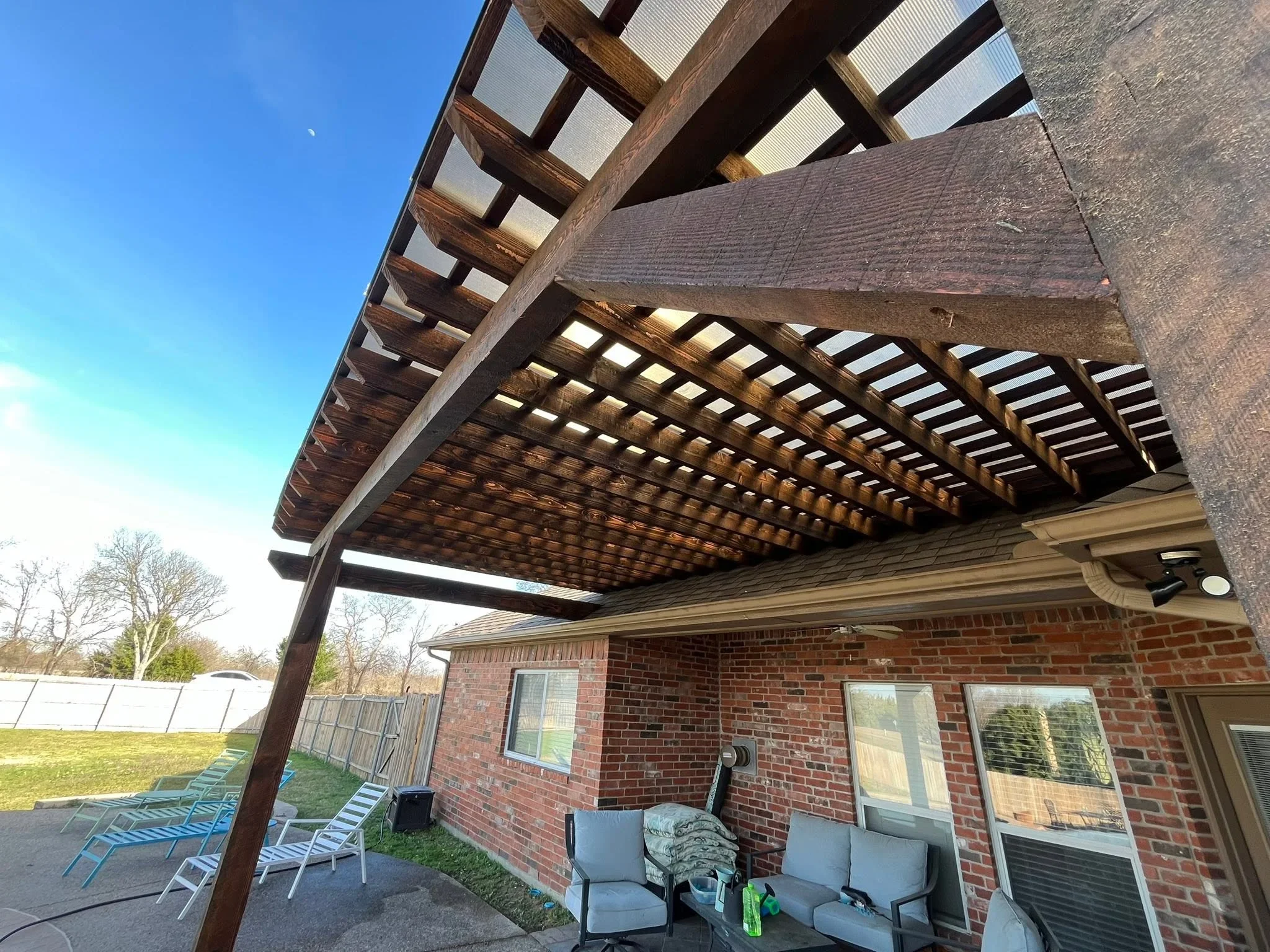 Dark stained wood pergola with adjustable louvered roof panels over brick patio
