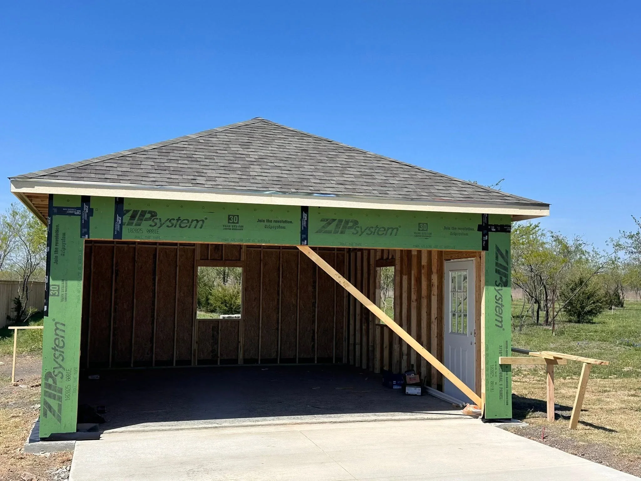 Wood-framed garage under construction with asphalt shingle roof and concrete pad