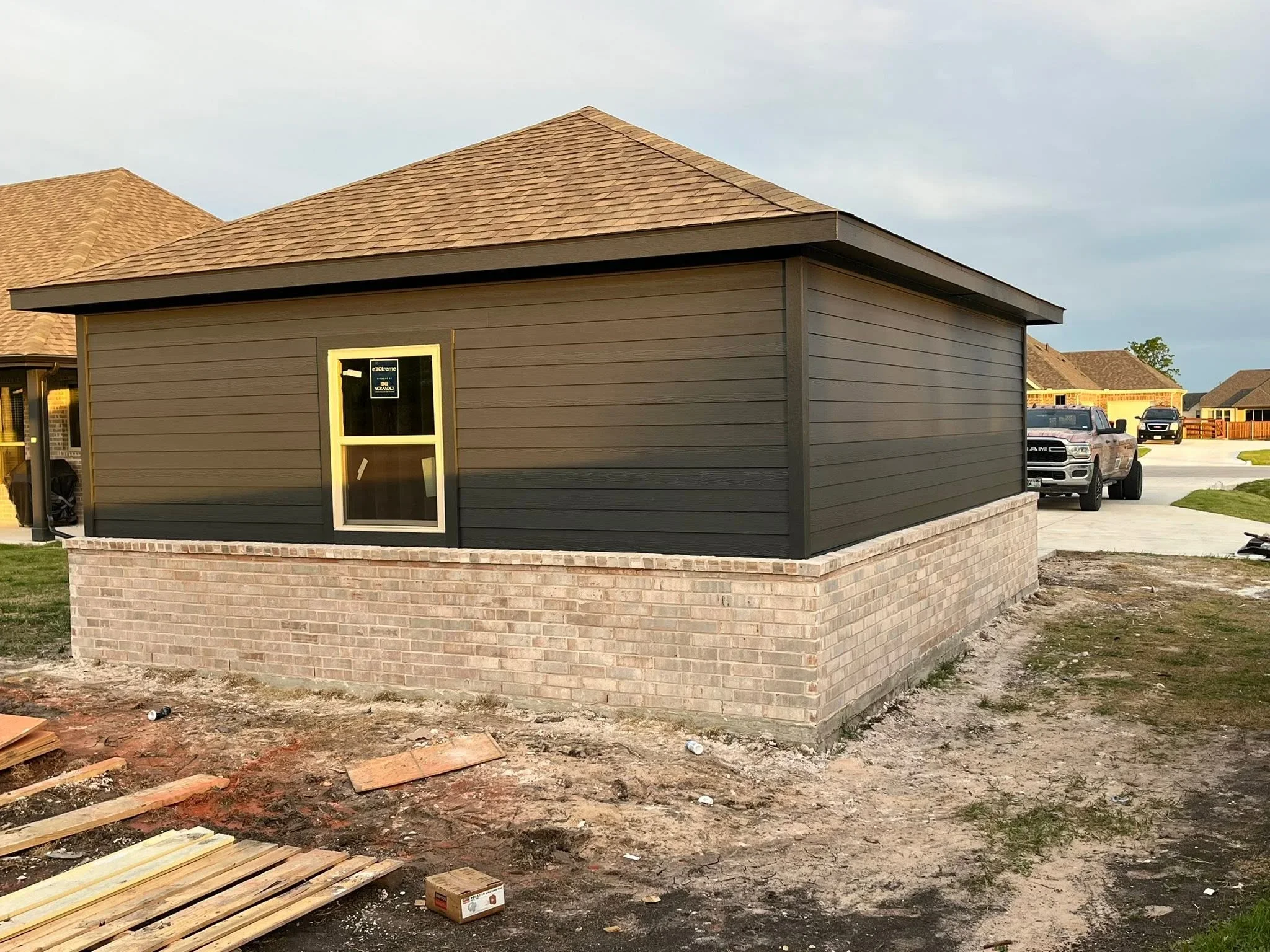 Charcoal gray horizontal siding garage with tan shingle roof and brick foundation