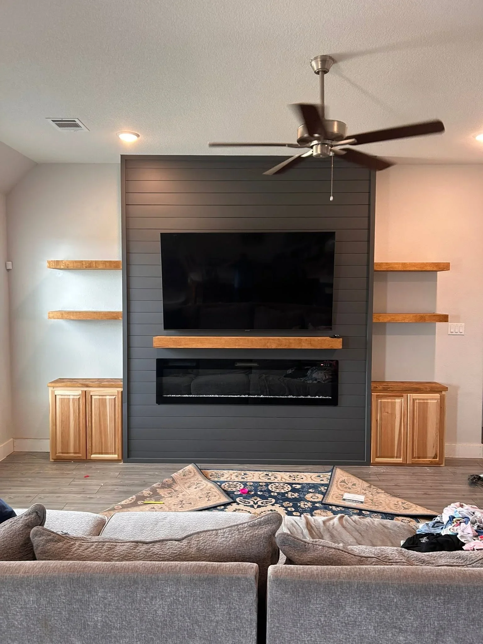 Gray shiplap entertainment wall with electric fireplace, wood shelves, and cabinetry