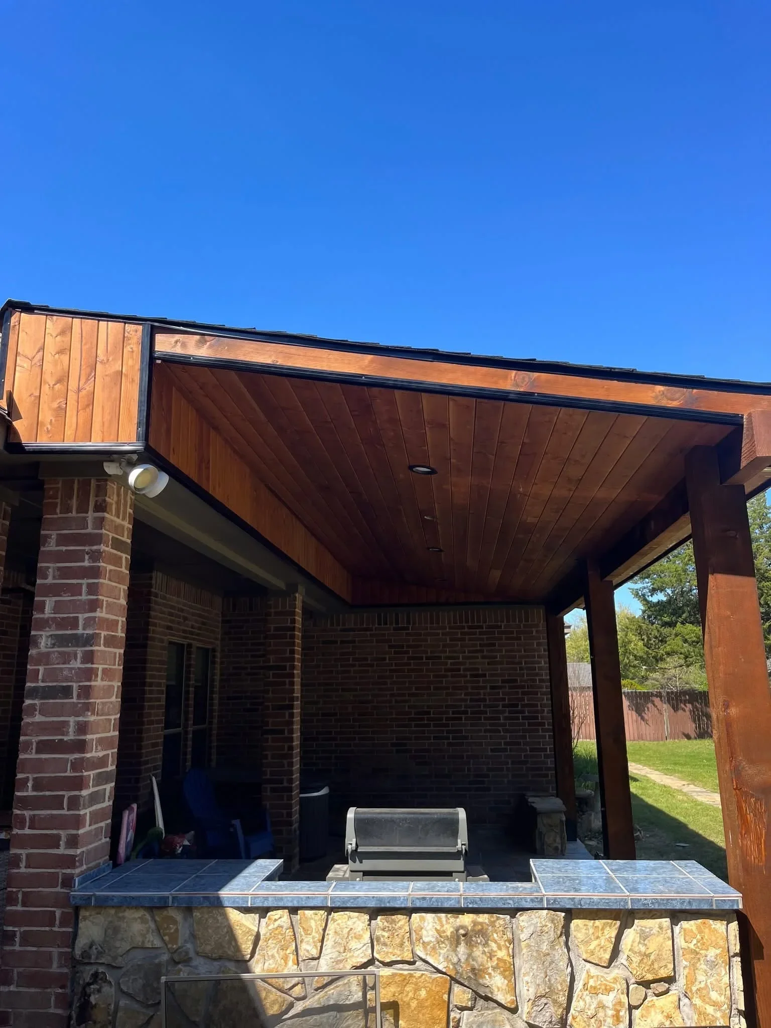 Cedar patio cover with black steel frame, stone base, and slate tile counter with built-in grill