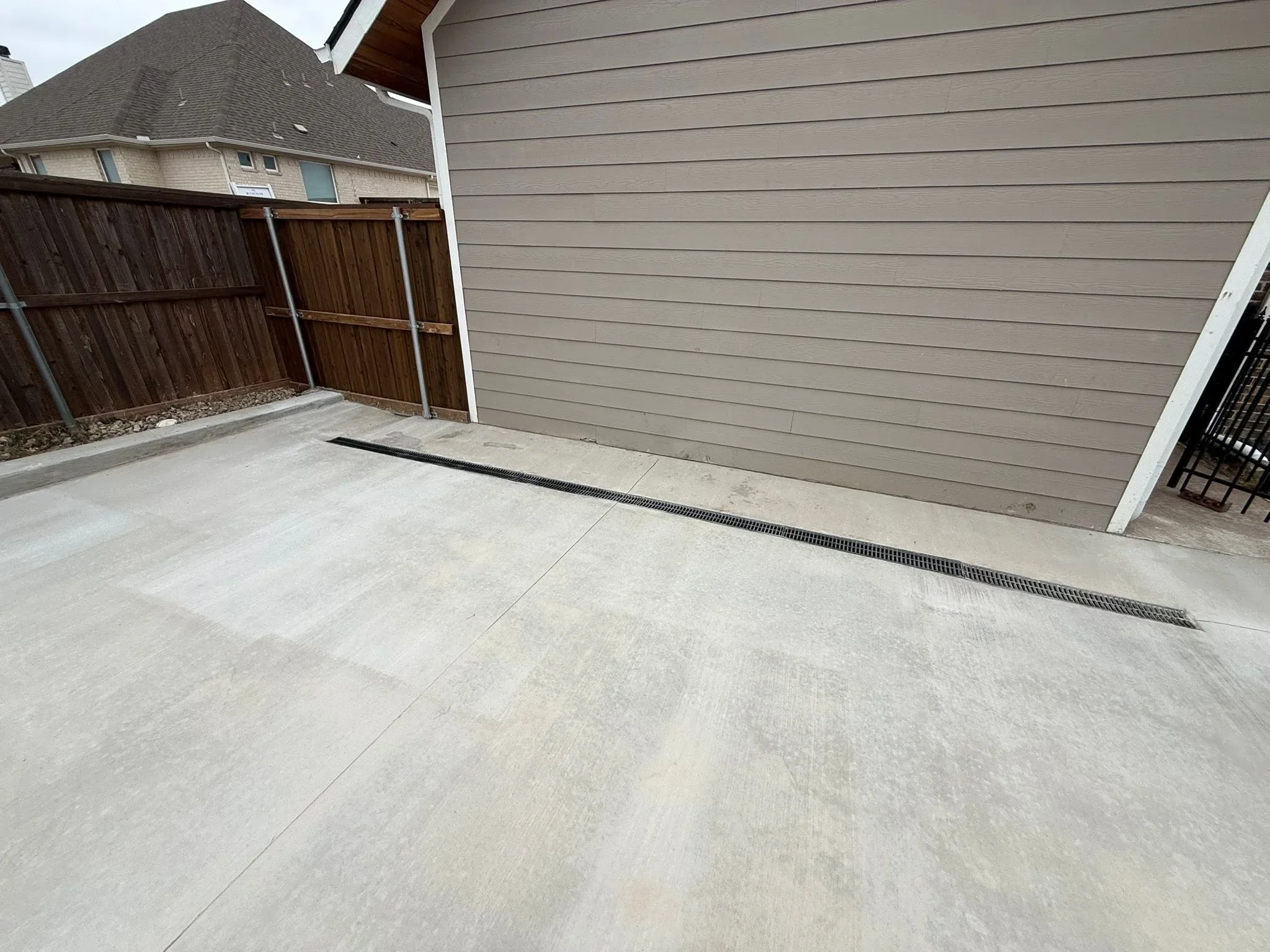 Concrete patio with linear drainage grate and wood fence perimeter