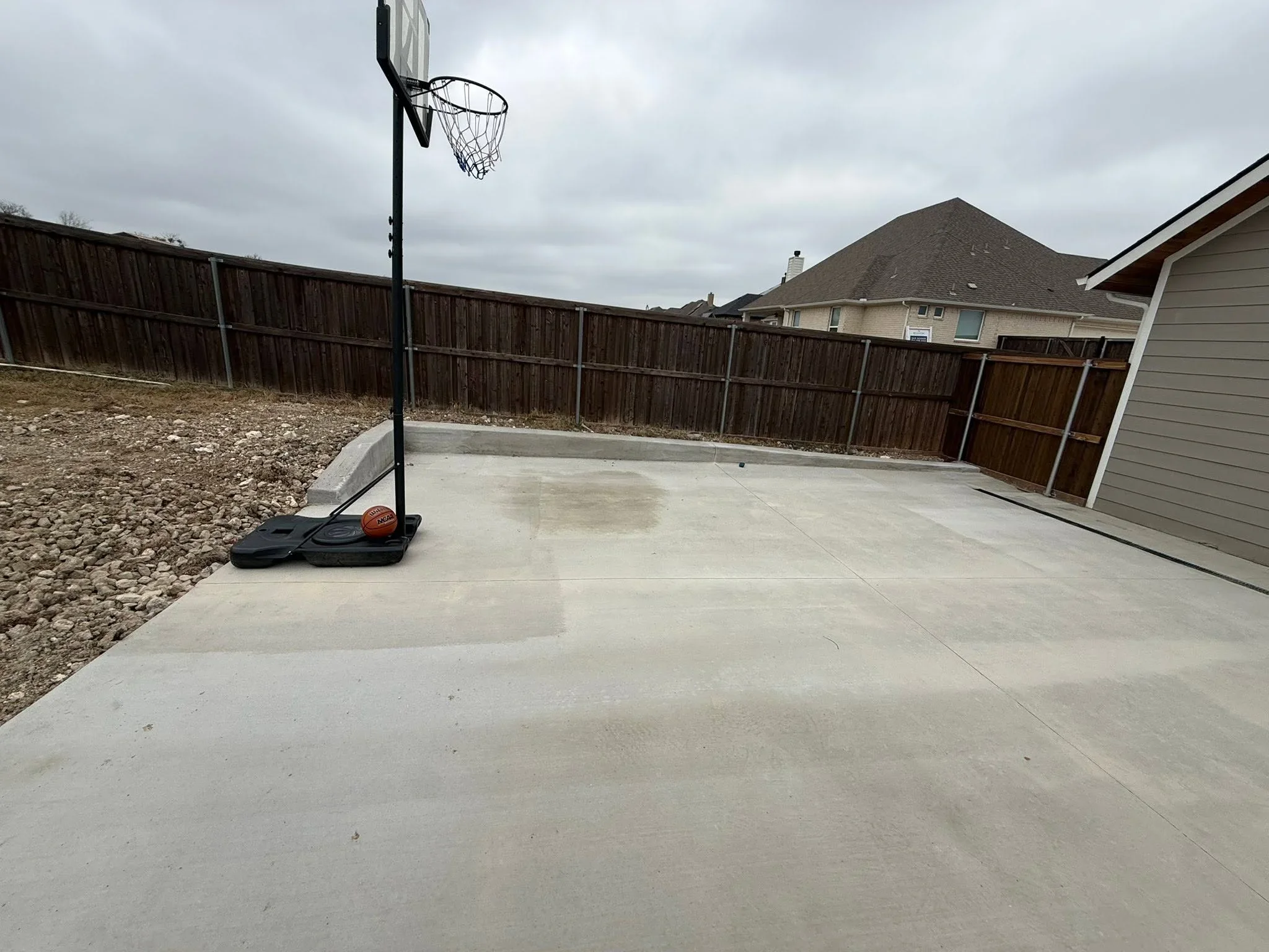 Concrete patio with basketball hoop and portable base in fenced residential backyard