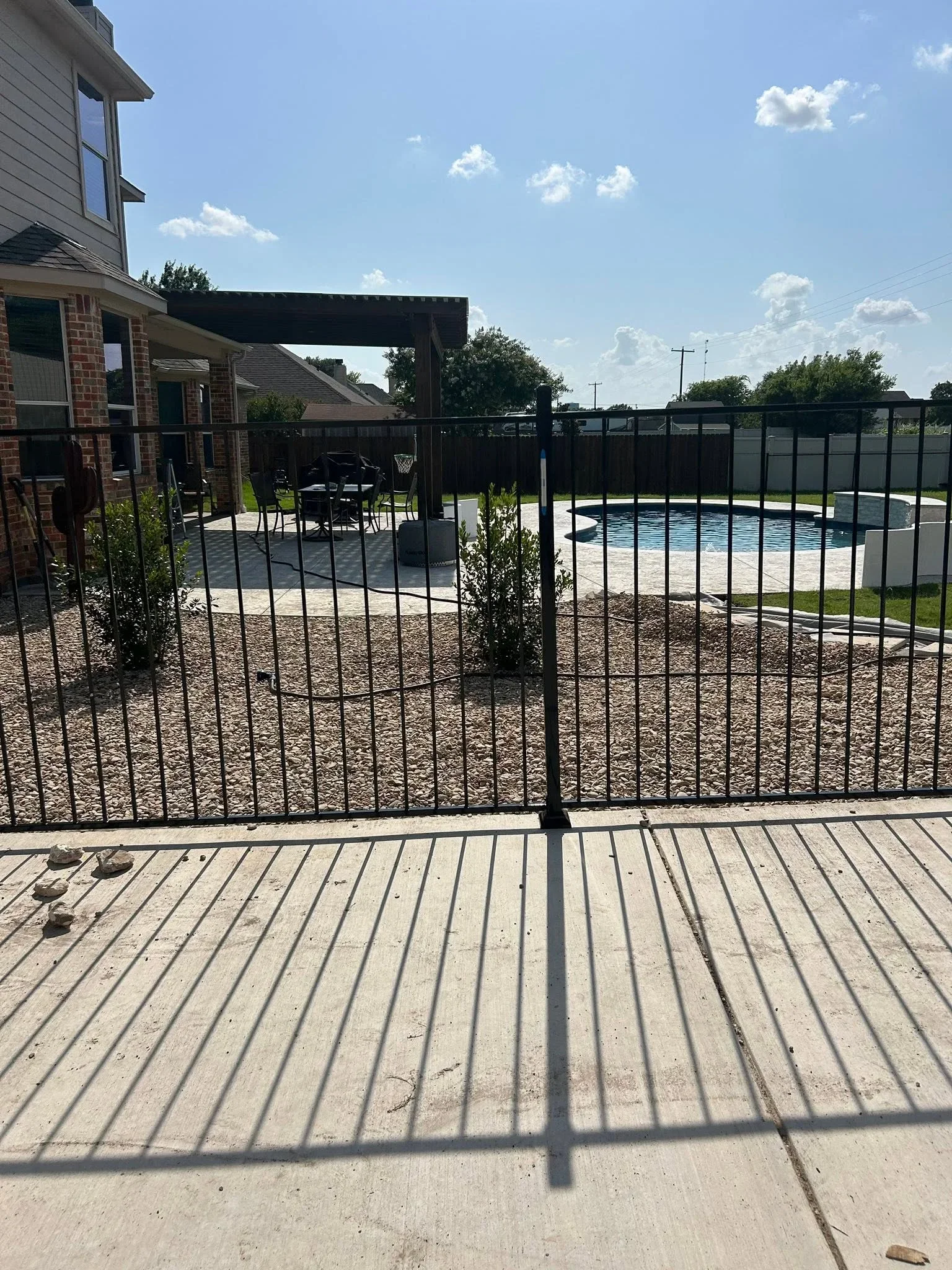 Black aluminum pool fence with vertical pickets around in-ground pool and concrete deck