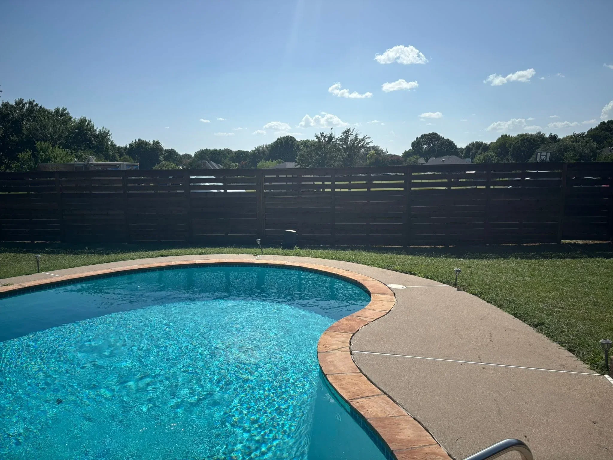 Dark horizontal slat privacy fence bordering pool deck and grassy yard