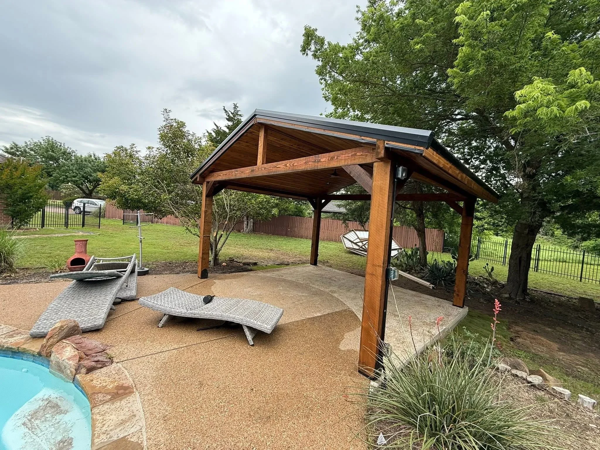 Wooden pavilion with timber frame, metal roof, and aggregate patio with cornhole boards
