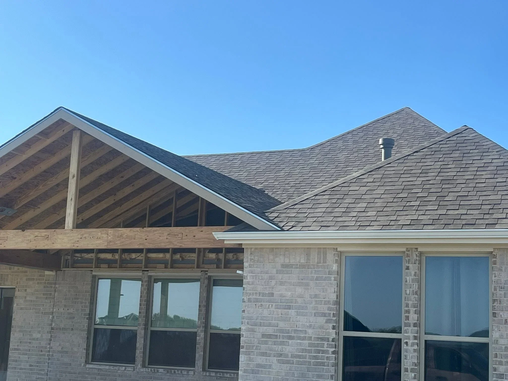 Gray architectural shingle roof with multiple pitches, exposed beams, and brick exterior
