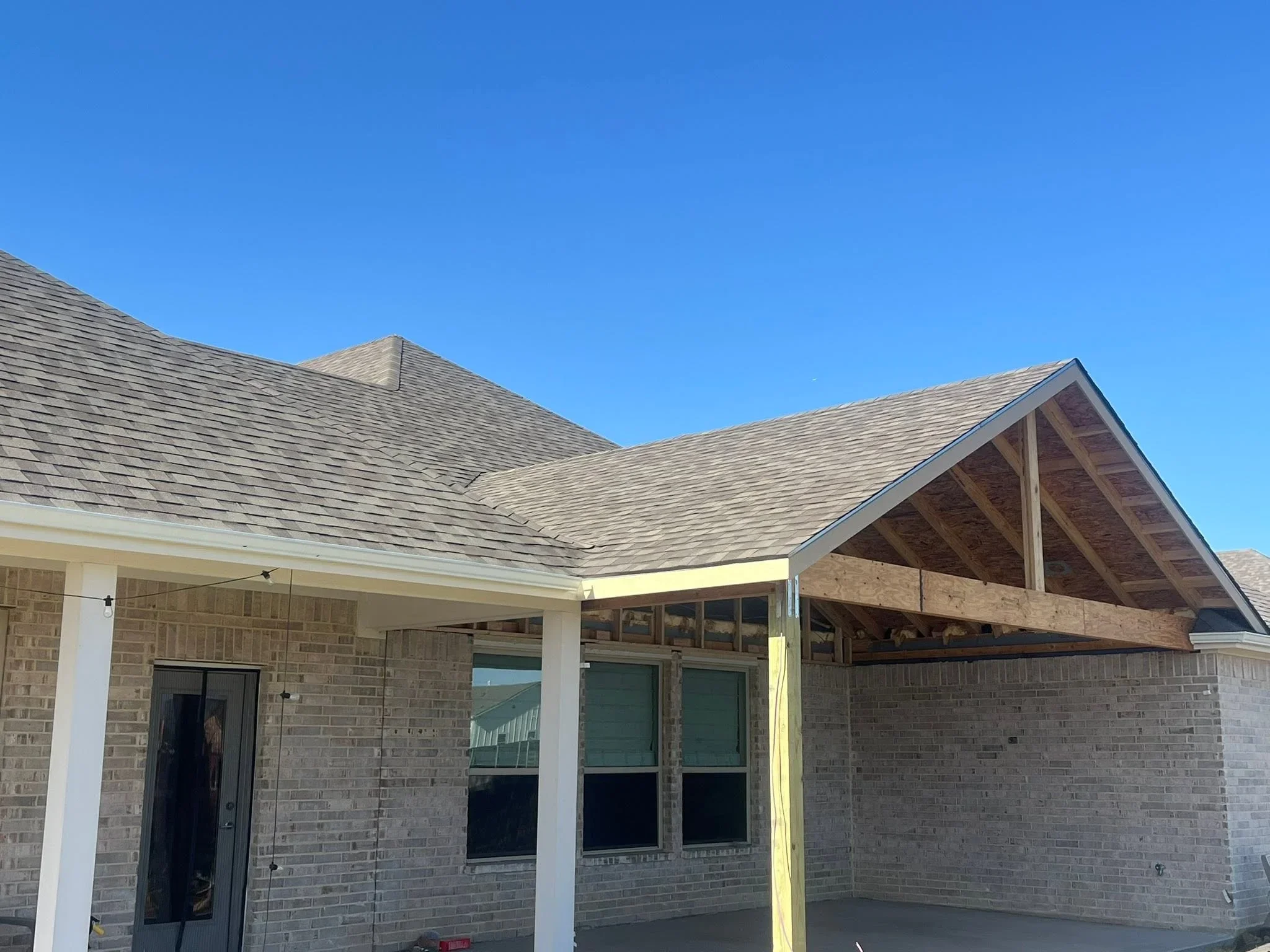 Gray architectural shingle roof with covered patio, white columns, and brick exterior