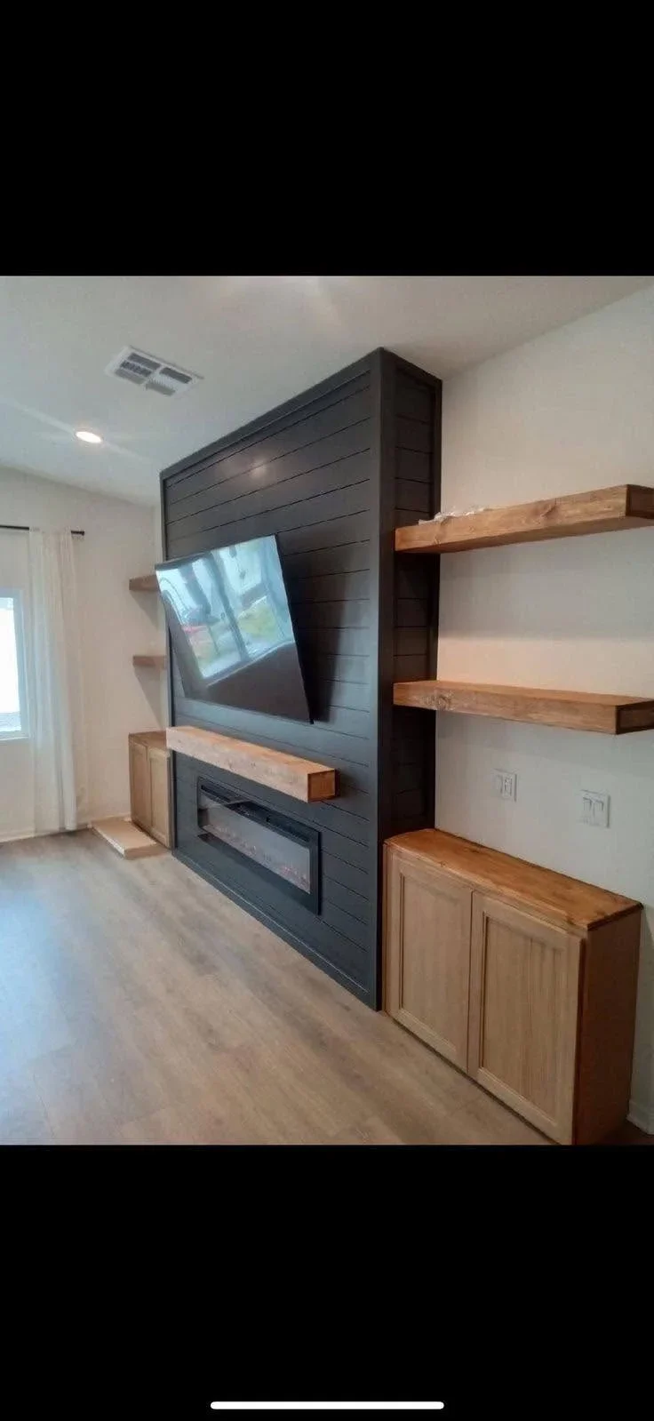 Dark shiplap entertainment wall with fireplace, mounted TV, wood shelves, and cabinetry