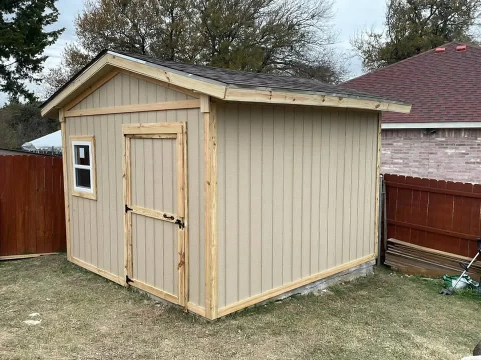 Tan metal-sided storage shed with gabled roof, wooden double doors, and window
