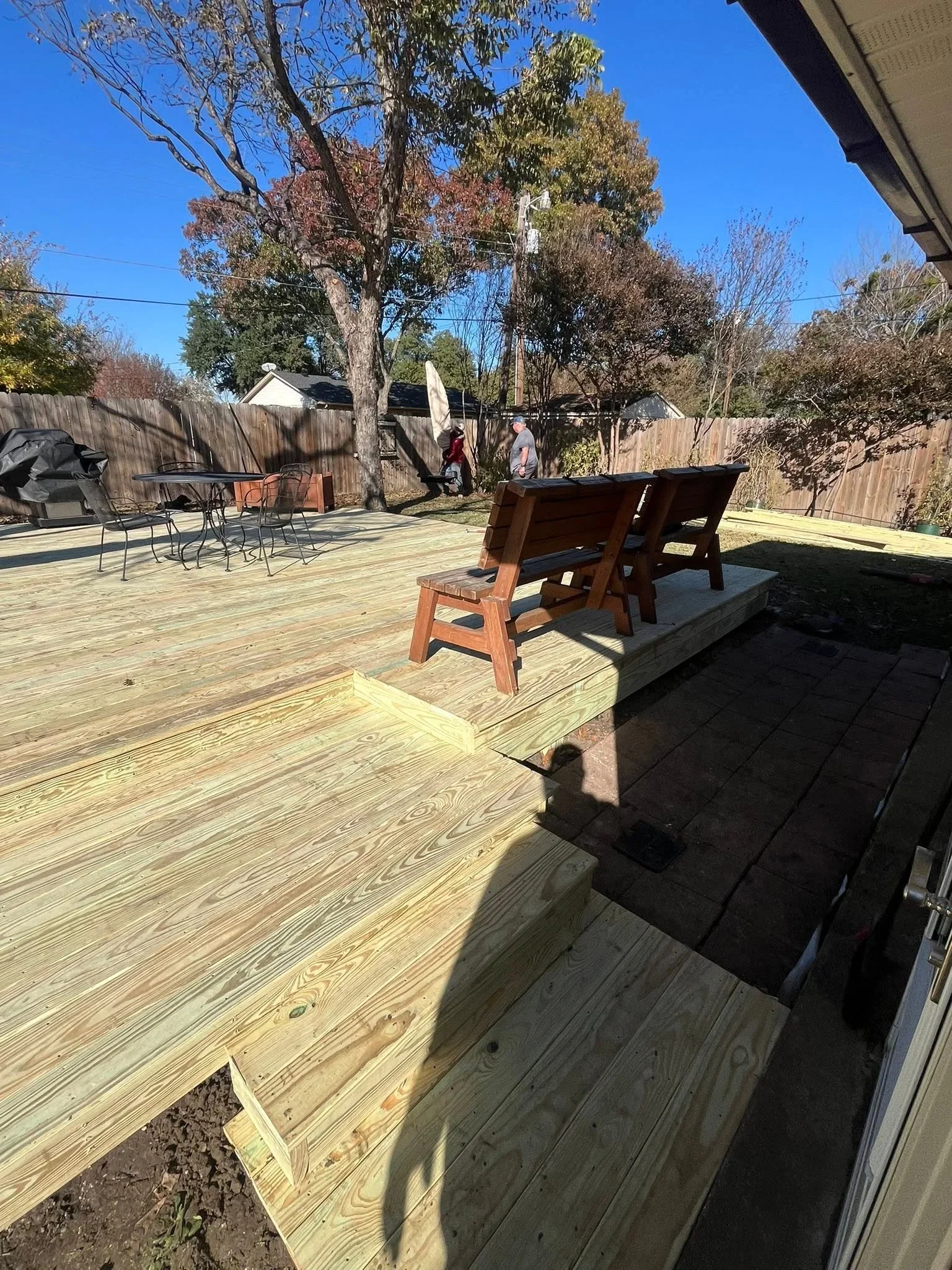 Pressure-treated wood deck with steps, multiple levels, and wood fence surrounding backyard