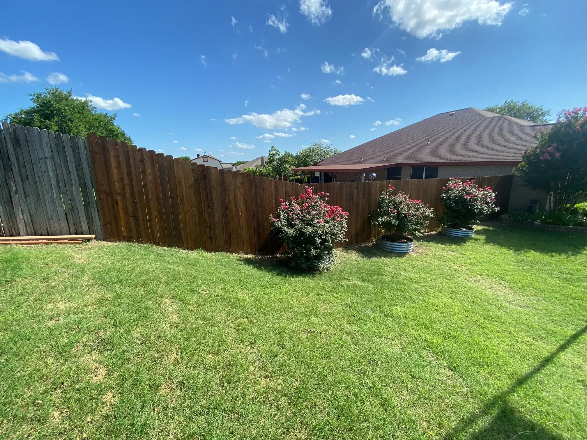 Brown stained wood privacy fence with vertical boards enclosing residential backyard with lawn