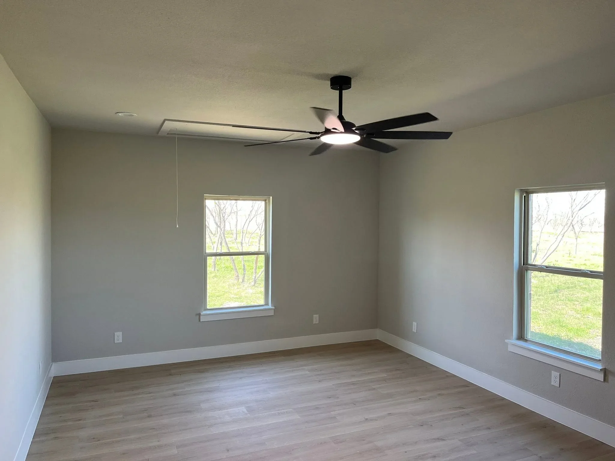 Finished interior room with gray drywall, white trim, wood flooring, and black ceiling fan