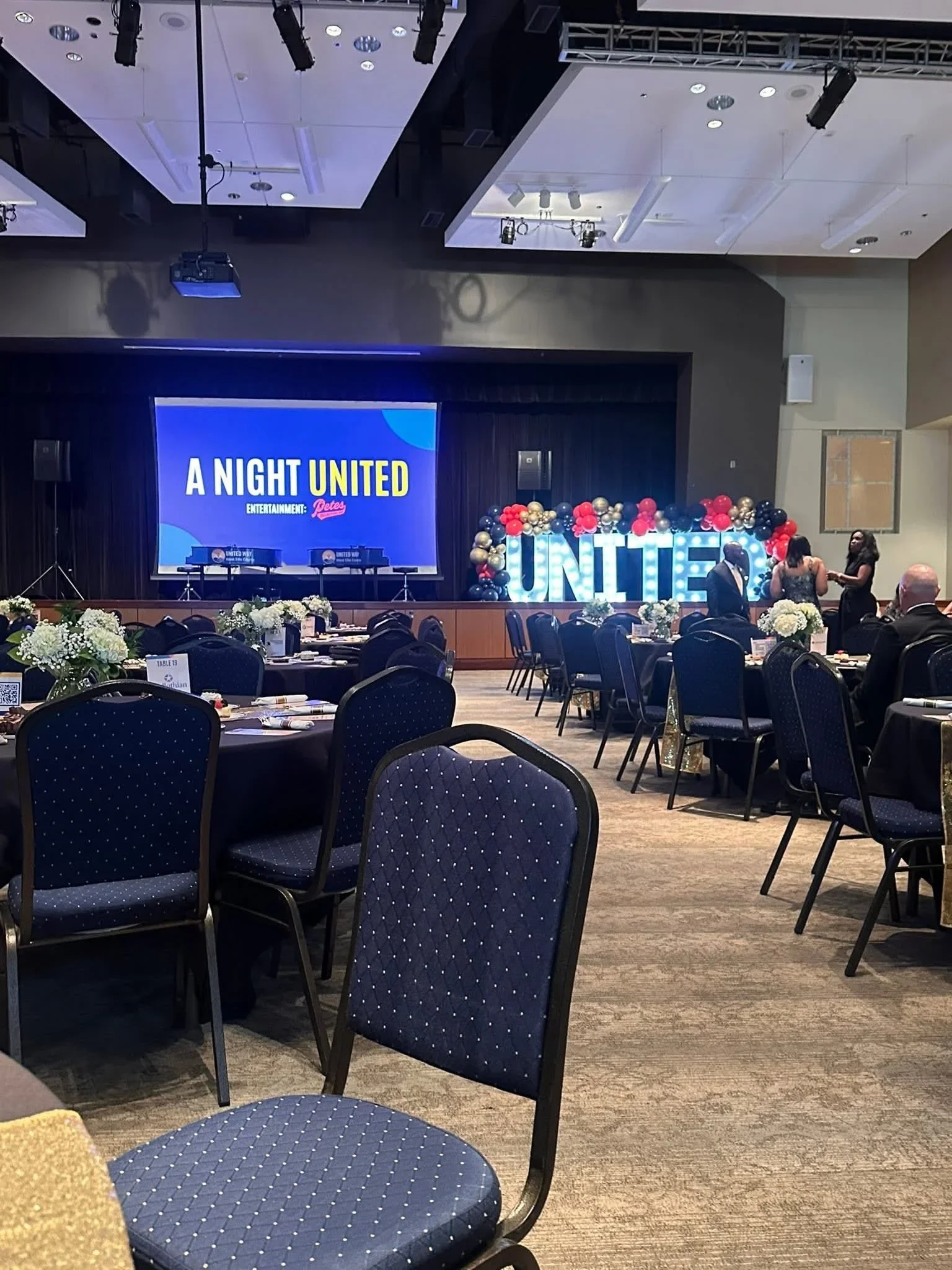 Event venue with recessed LED ceiling lights, track lighting, projection screen, and professional audio setup