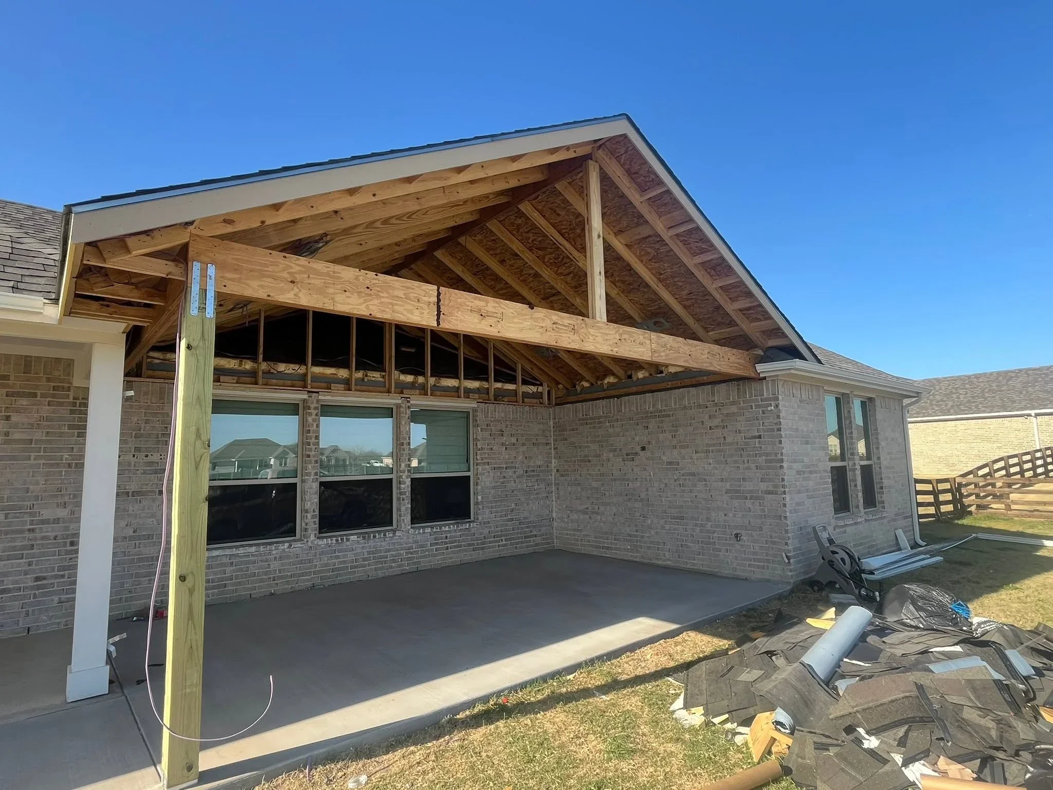Timber frame patio cover with exposed beams, gabled roof, and multi-pane windows over concrete pad