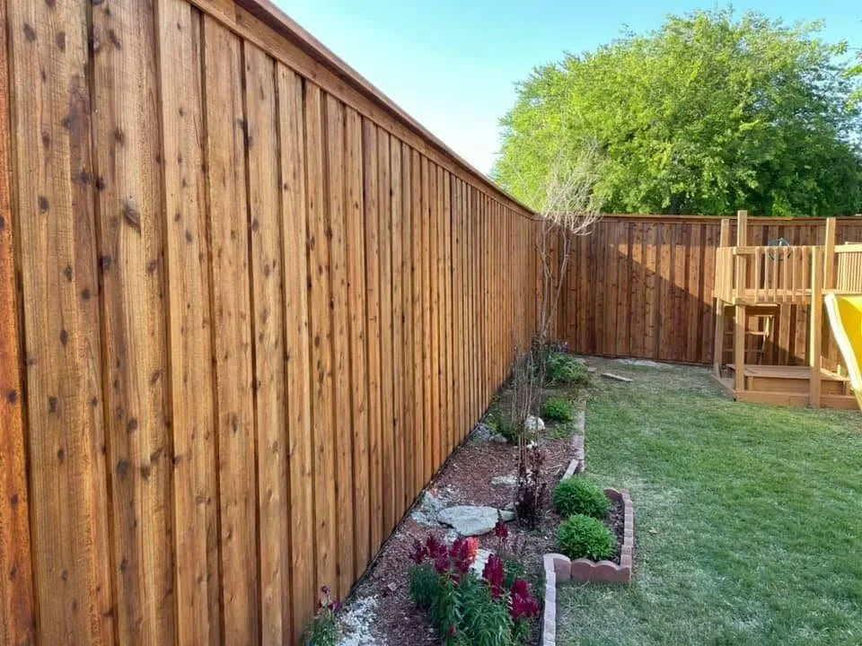Stained wood privacy fence with vertical boards and integrated landscape bed with plants and mulch
