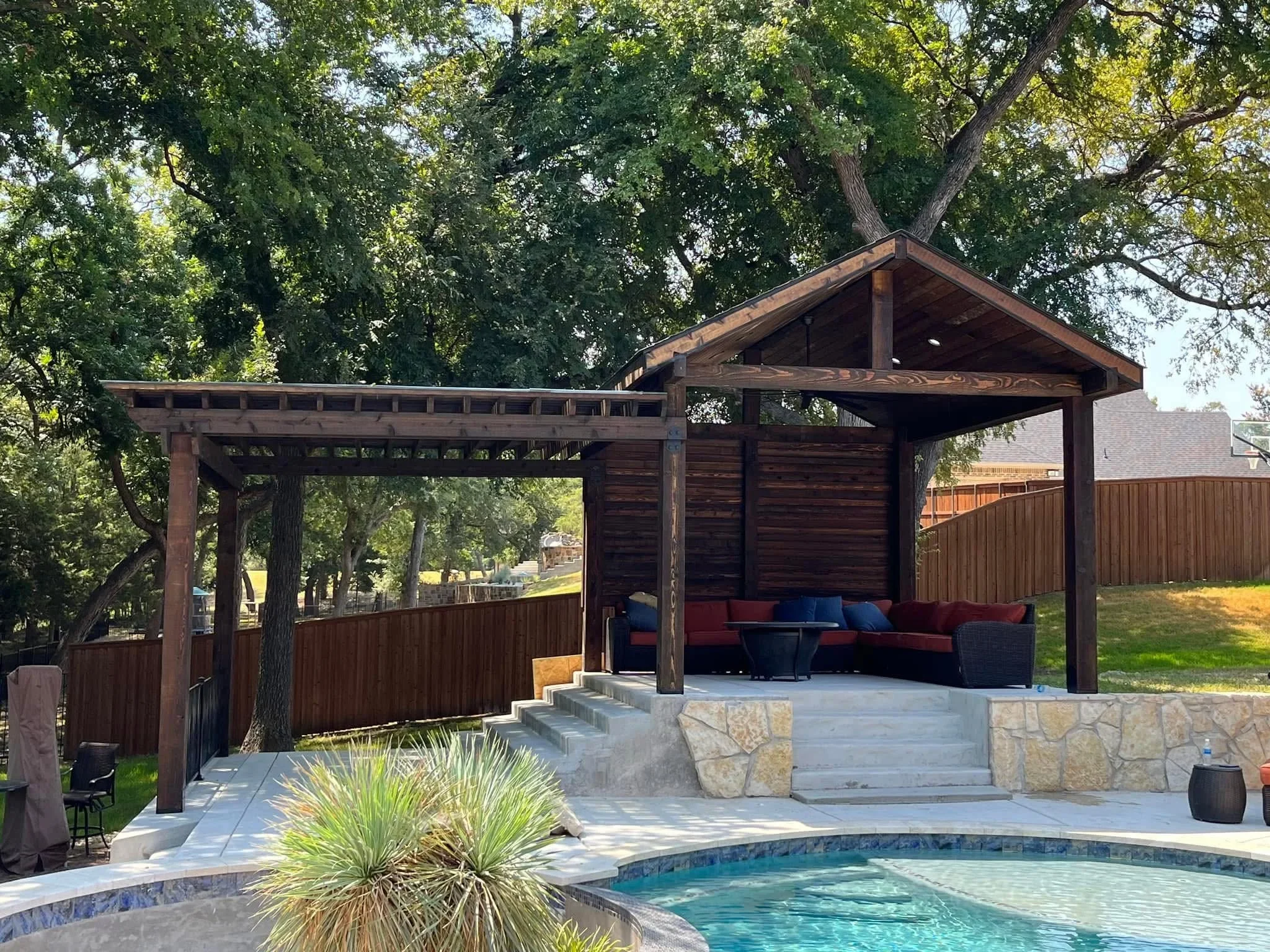 Stained wood pergola and privacy fence with horizontal slats surrounding pool area with stone walls