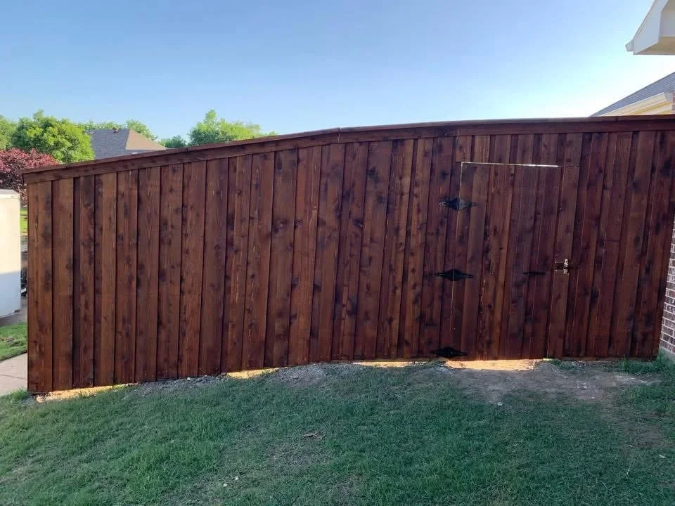 Dark stained wood privacy fence with vertical boards and double gate with black hardware