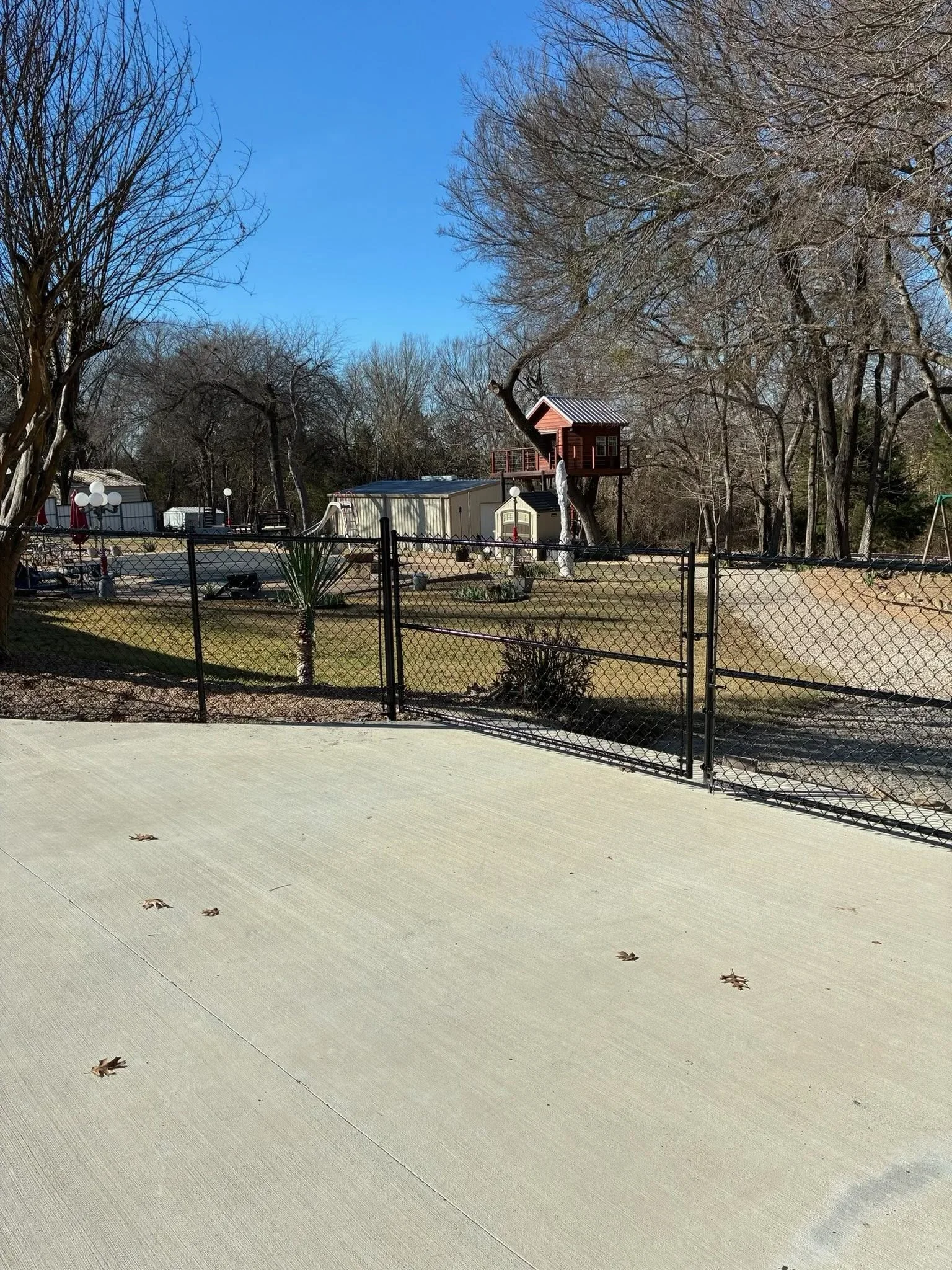 Black chain-link fence with gate around residential property, concrete pad in foreground