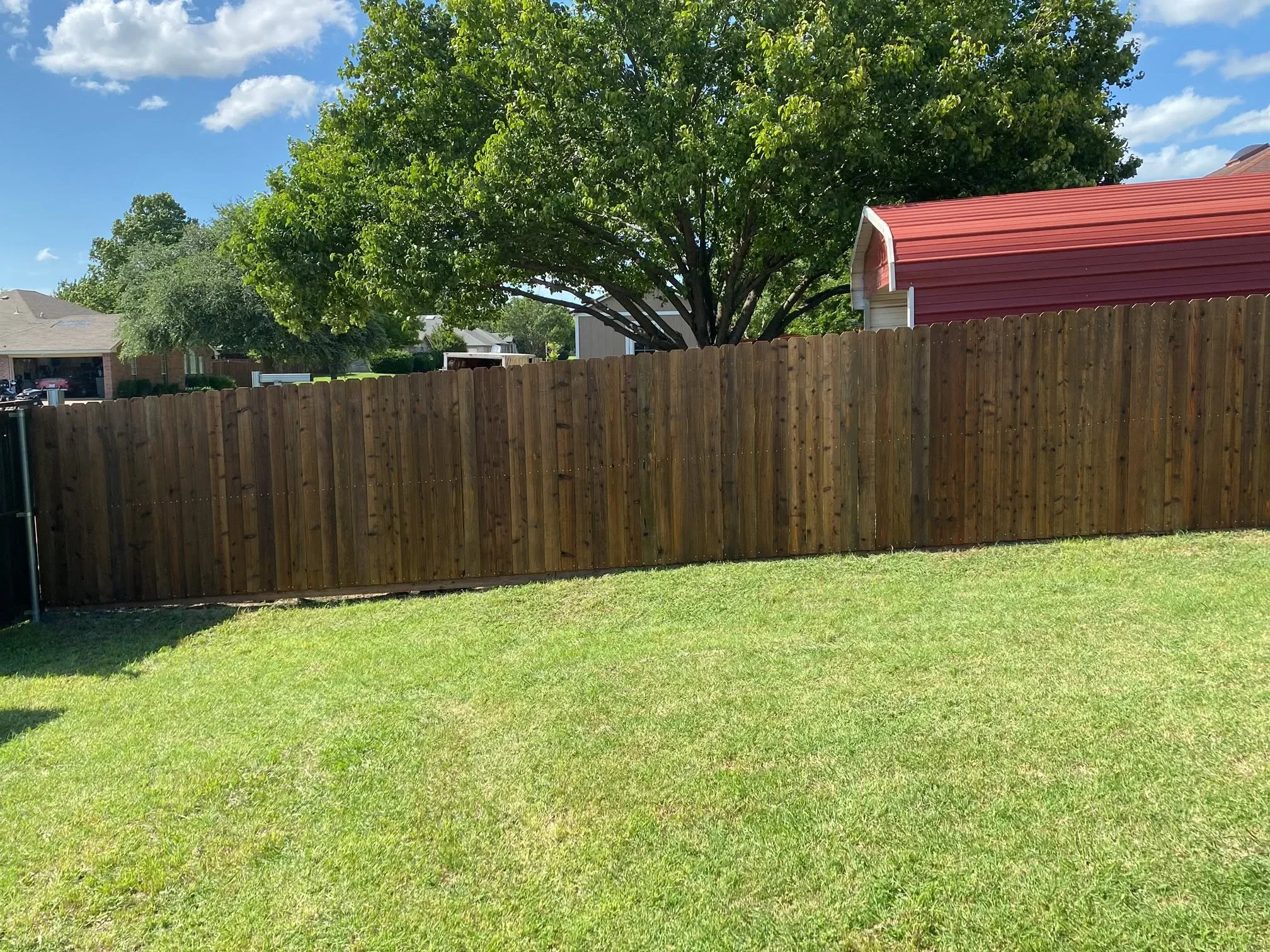 Pressure-treated wood privacy fence with vertical pickets installed along residential backyard property line