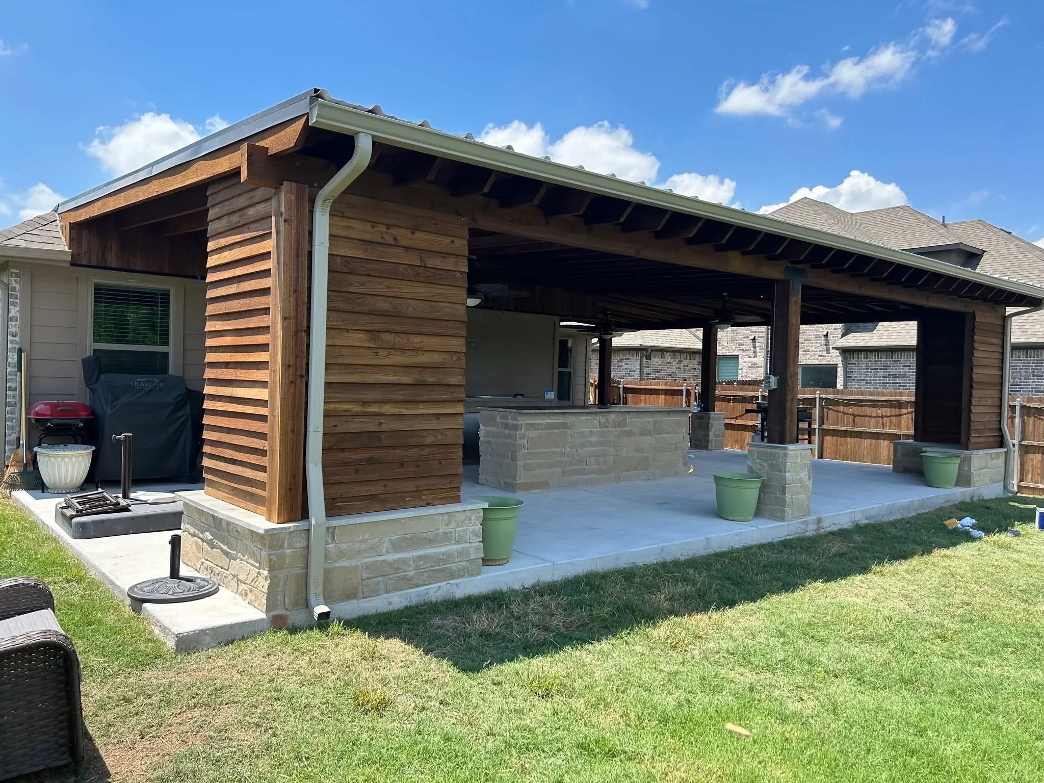 Covered patio with concrete slab, stone veneer base, horizontal wood siding, and steel beam structure