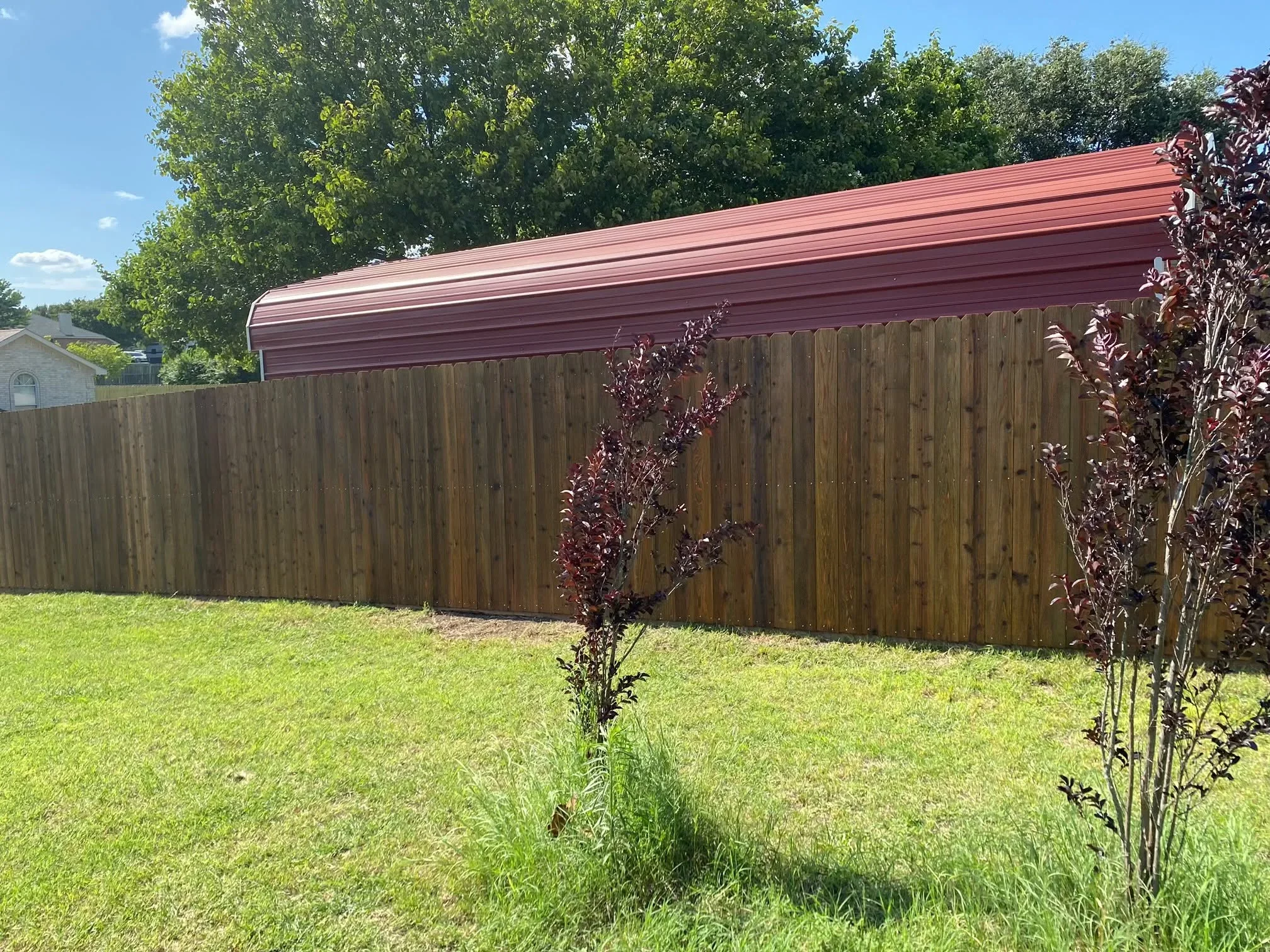 Wood privacy fence with vertical boards and corrugated metal roof structure in residential yard