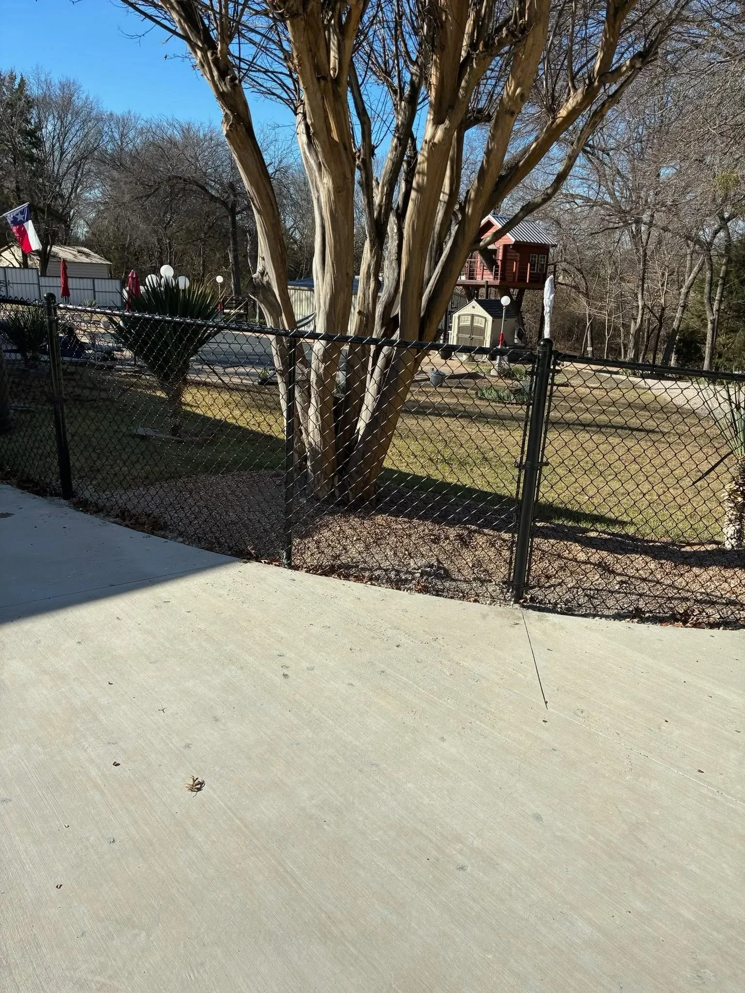 Black chain-link fence with gate installed around residential yard with mature trees
