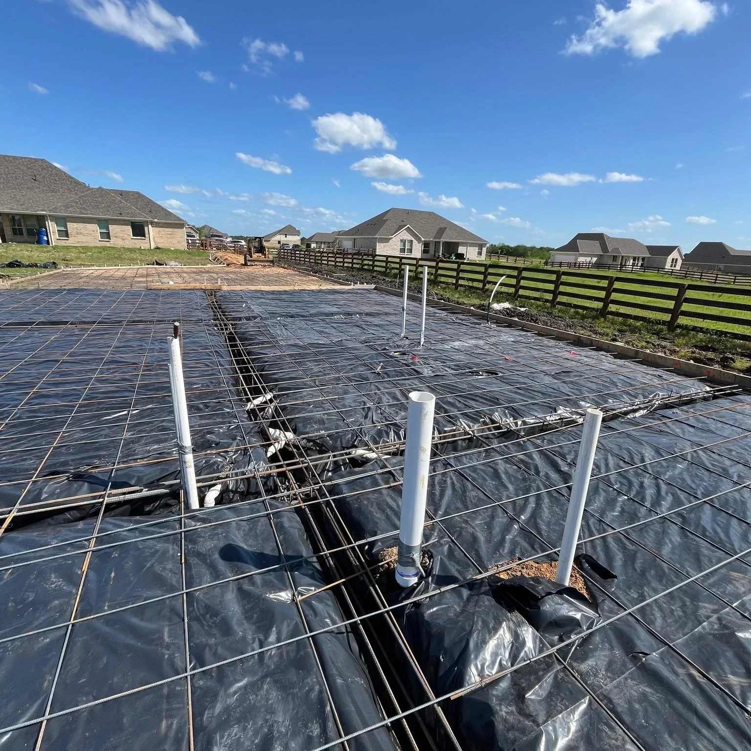 Black landscape fabric with rebar grid and white posts on prepared foundation site