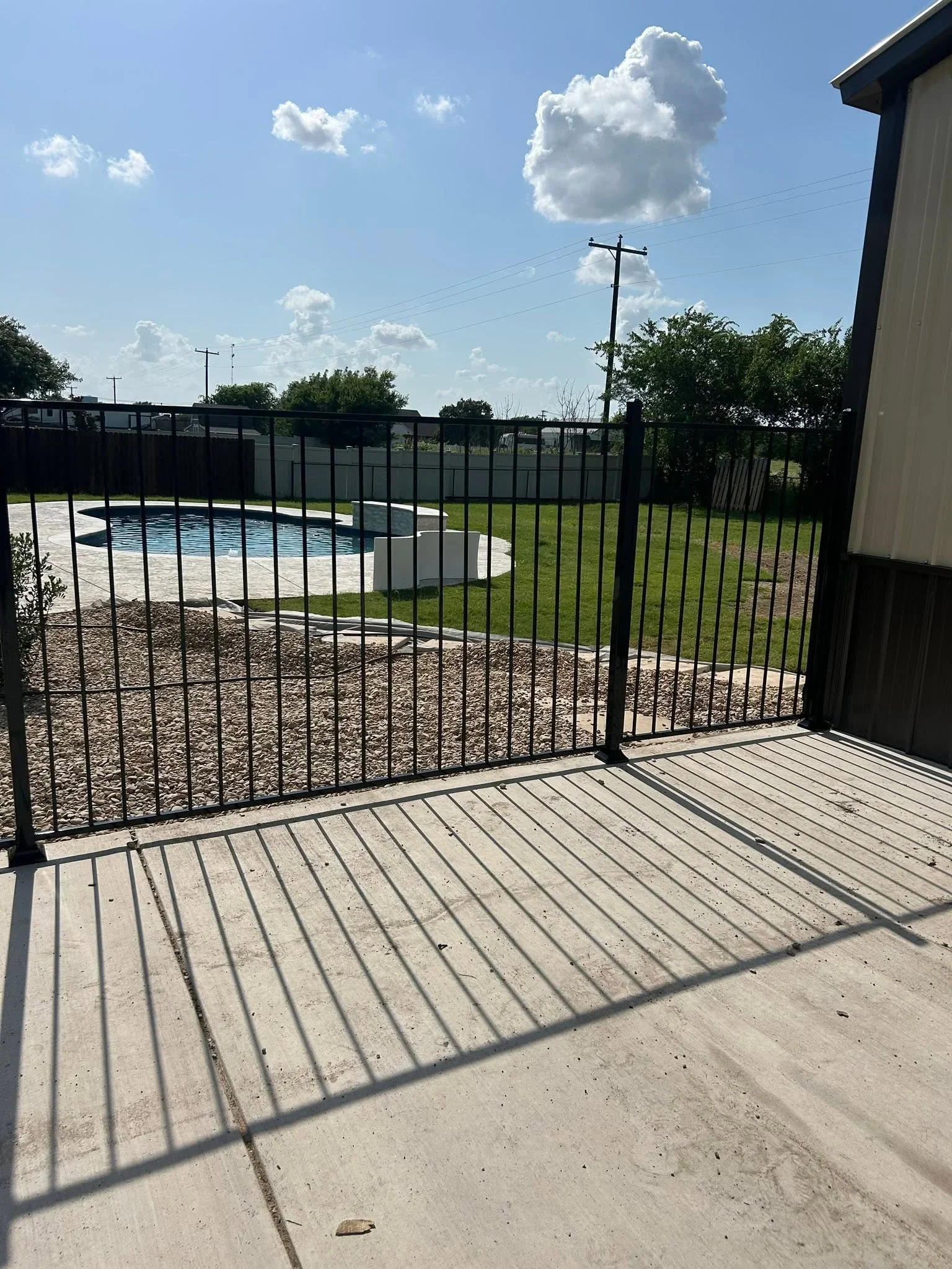 Black aluminum pool safety fence with gate around in-ground pool, concrete pad and gravel base