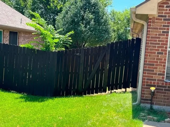 Black vertical board privacy fence with brick home and green lawn