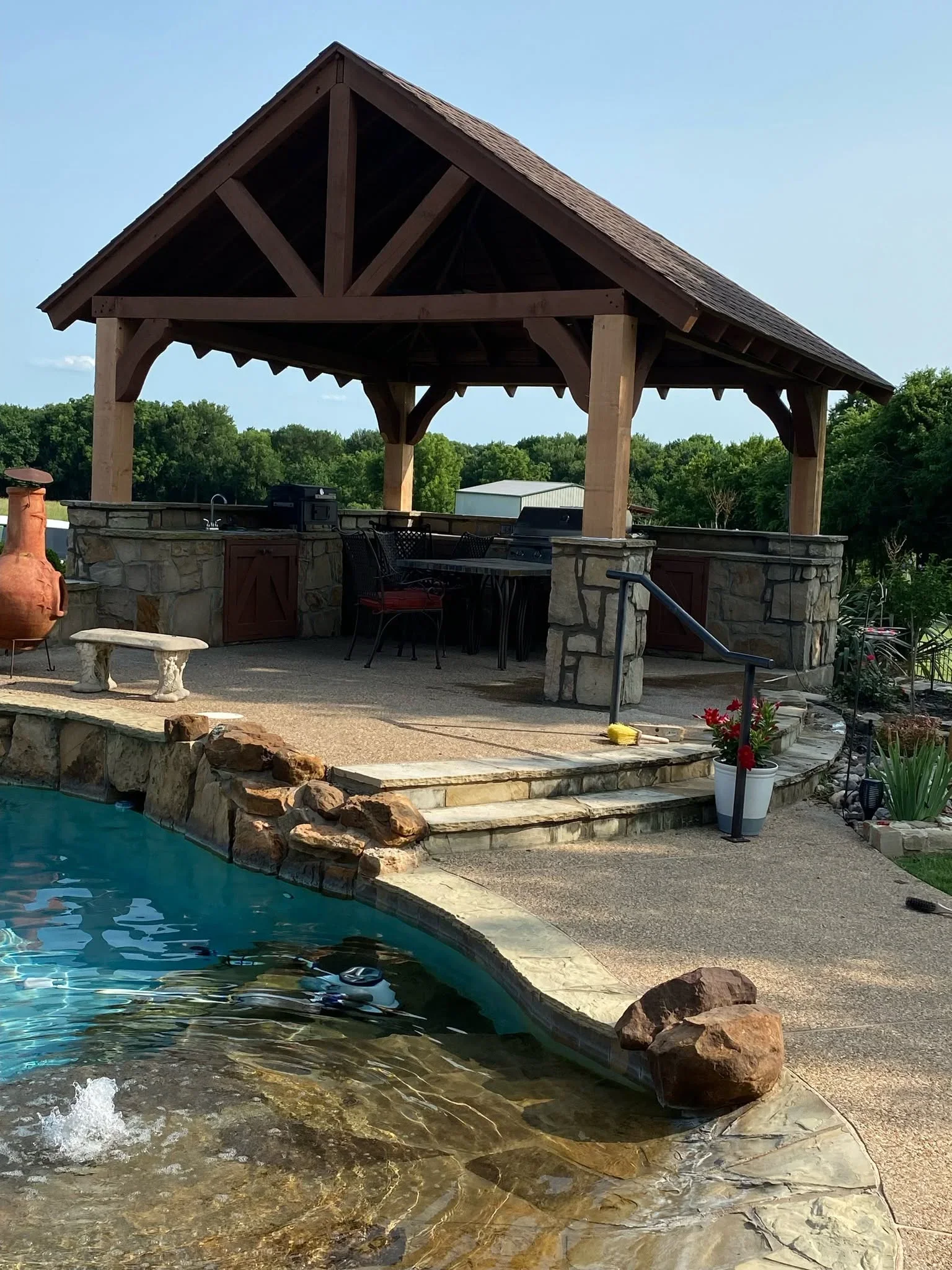 Timber pavilion with gabled roof over stone patio and pool edge