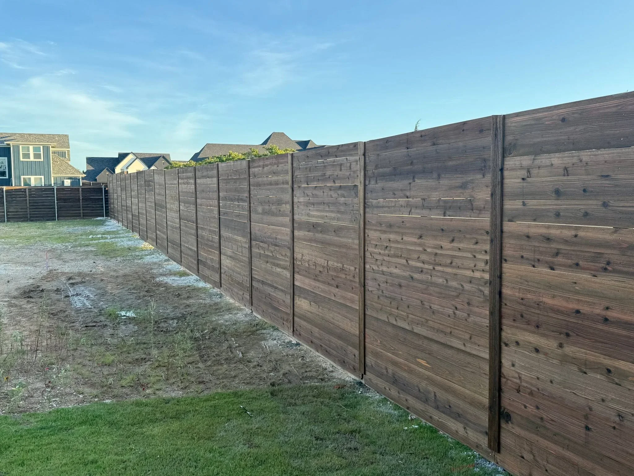 Horizontal wood privacy fence with stained timber boards and metal posts in residential backyard