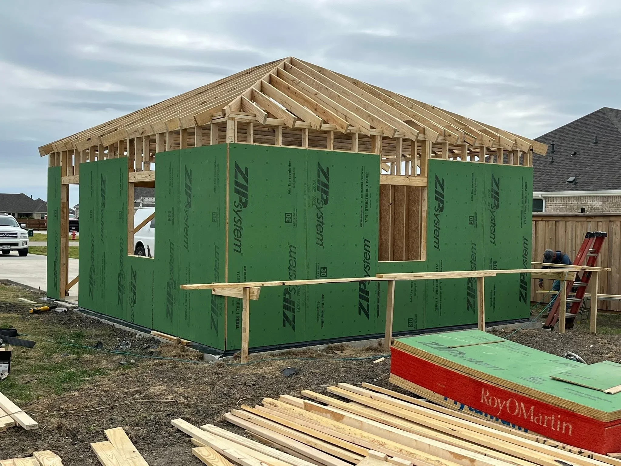 Wood-framed house under construction with green housewrap and exposed roof trusses