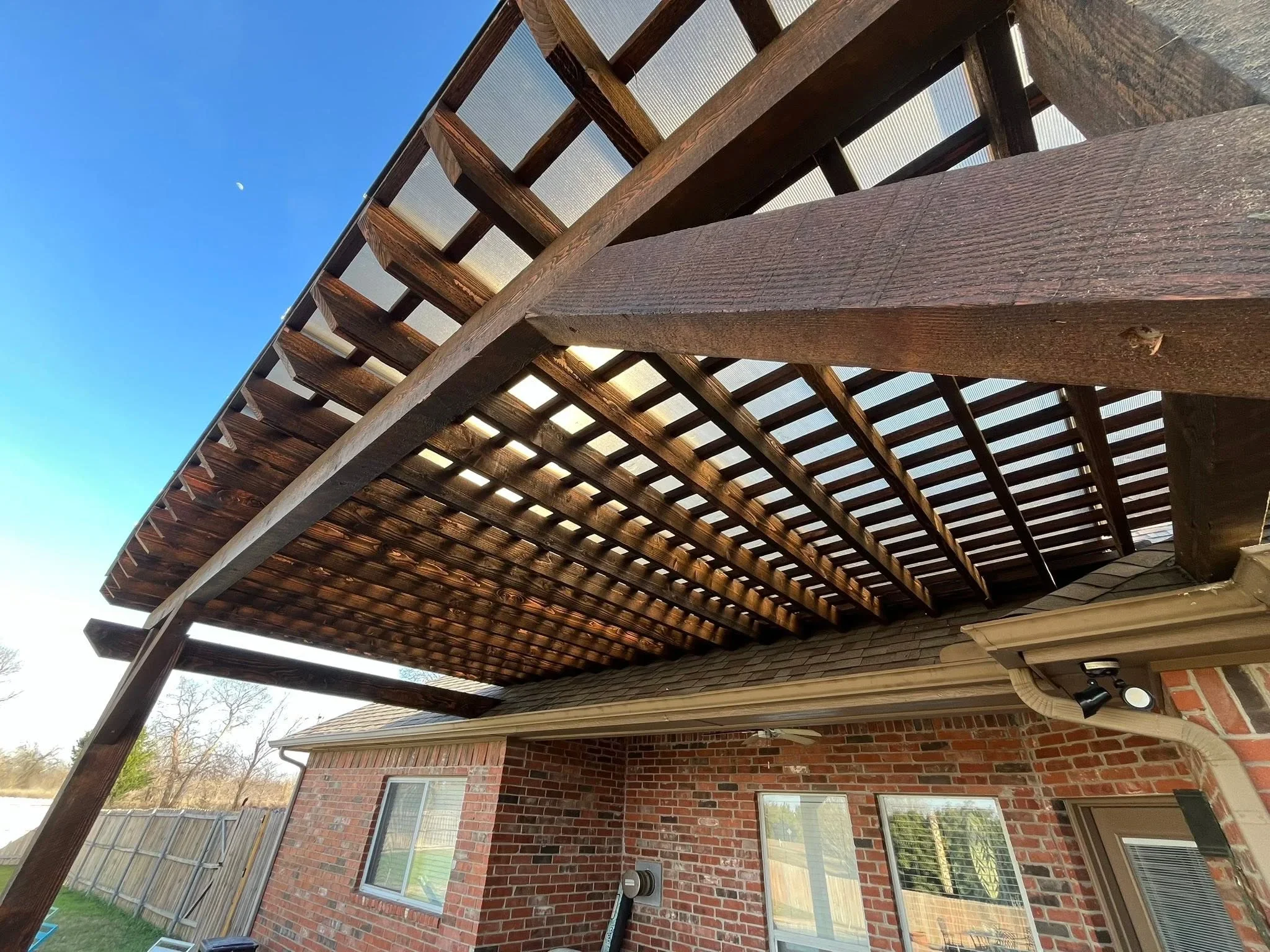 Stained wood pergola with polycarbonate panels attached to brick home exterior