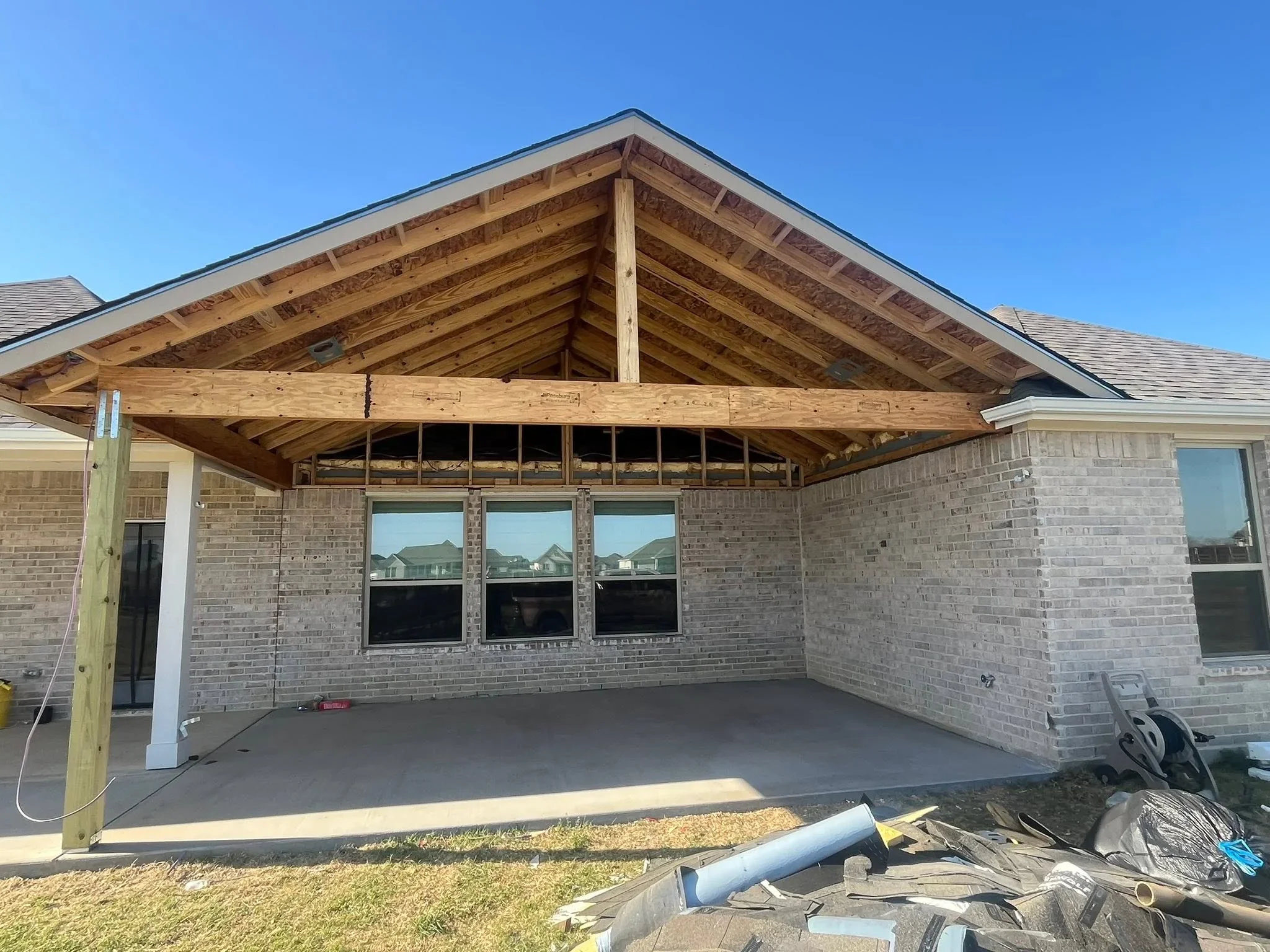 Covered patio with exposed wood beam framing, gabled roof, brick walls, and concrete floor