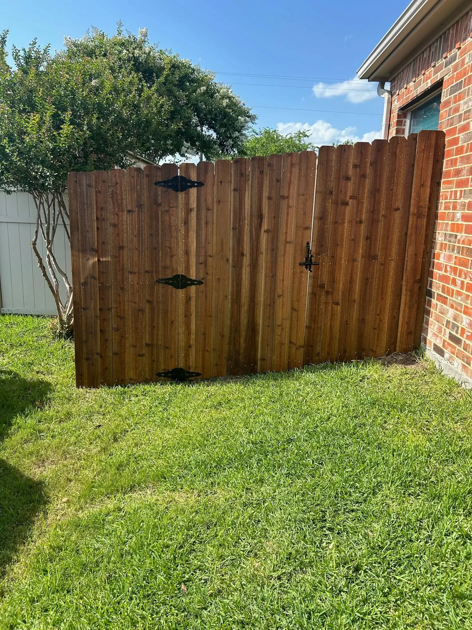 Stained wooden privacy fence with vertical boards and black hardware gate hinges