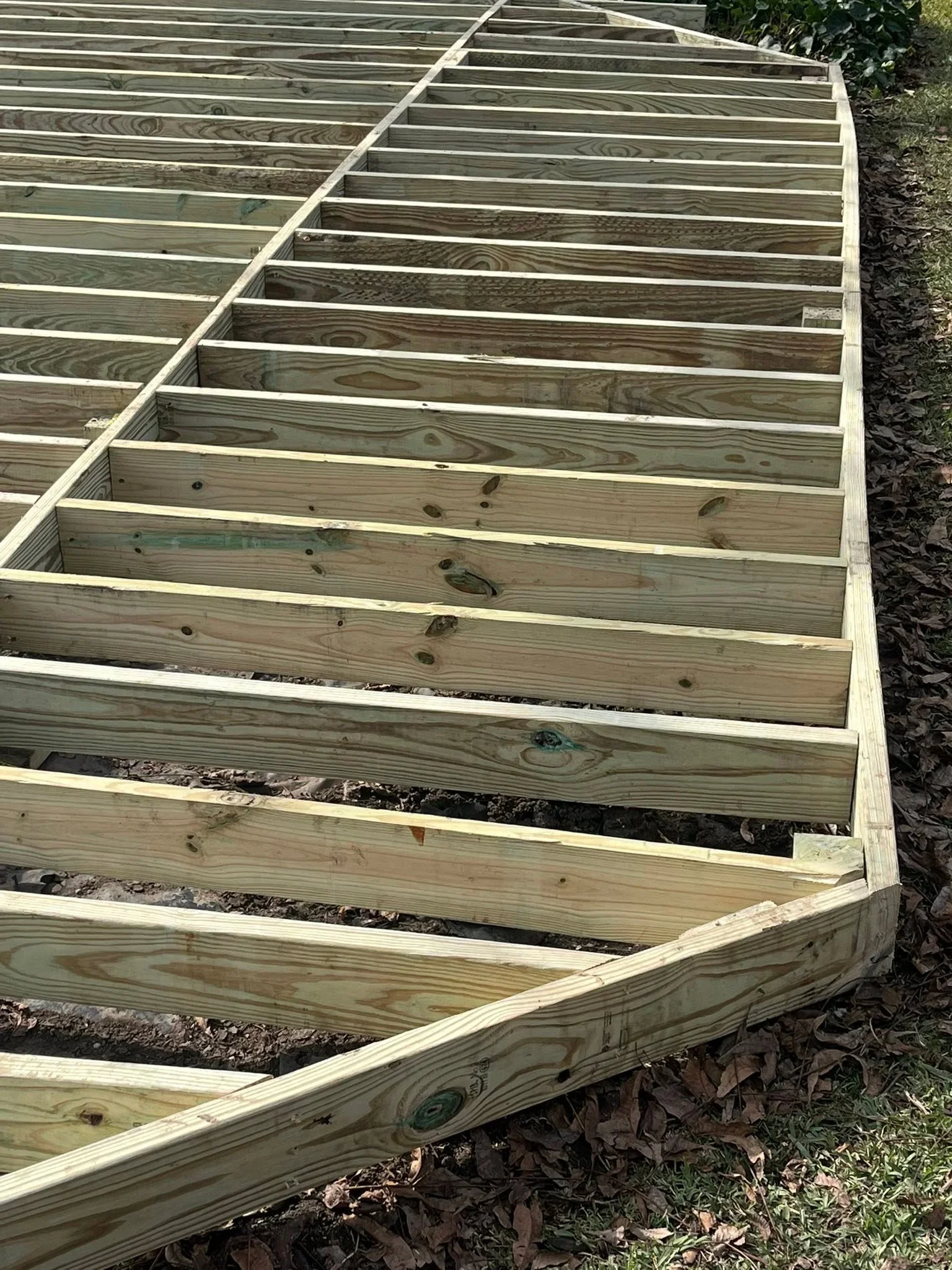 Pressure-treated wood deck frame with parallel joists and support beams during construction