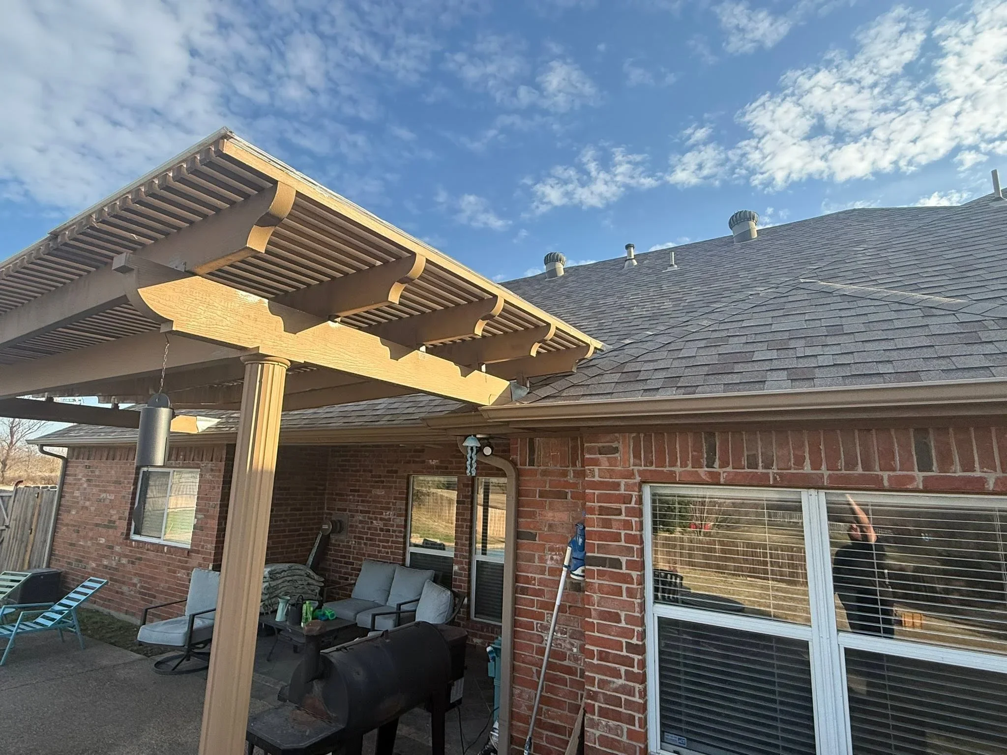 Wood pergola with horizontal slats and brackets over brick patio area