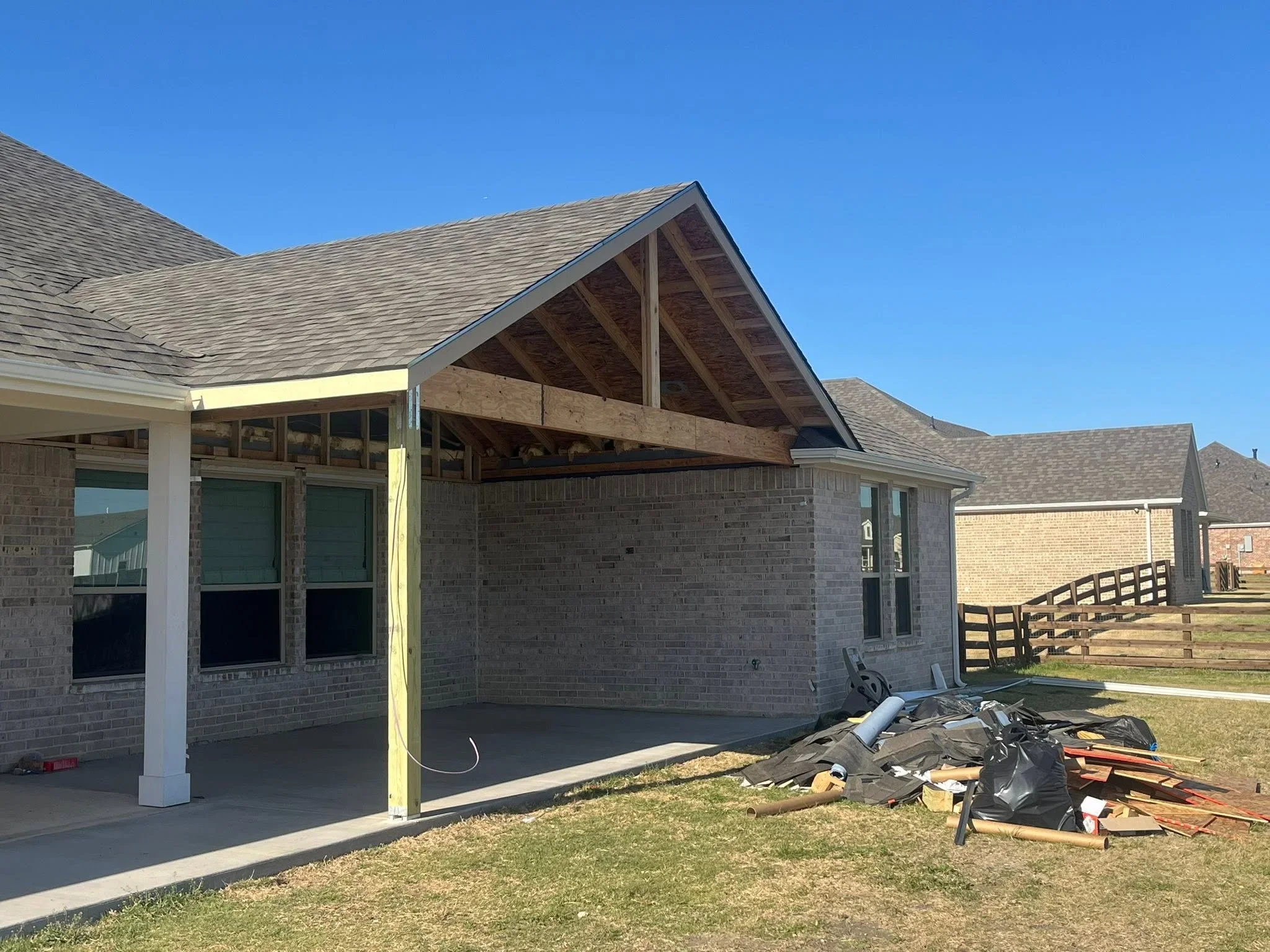 Brick home addition with gabled roof, exposed beams, covered patio, white columns, and concrete foundation