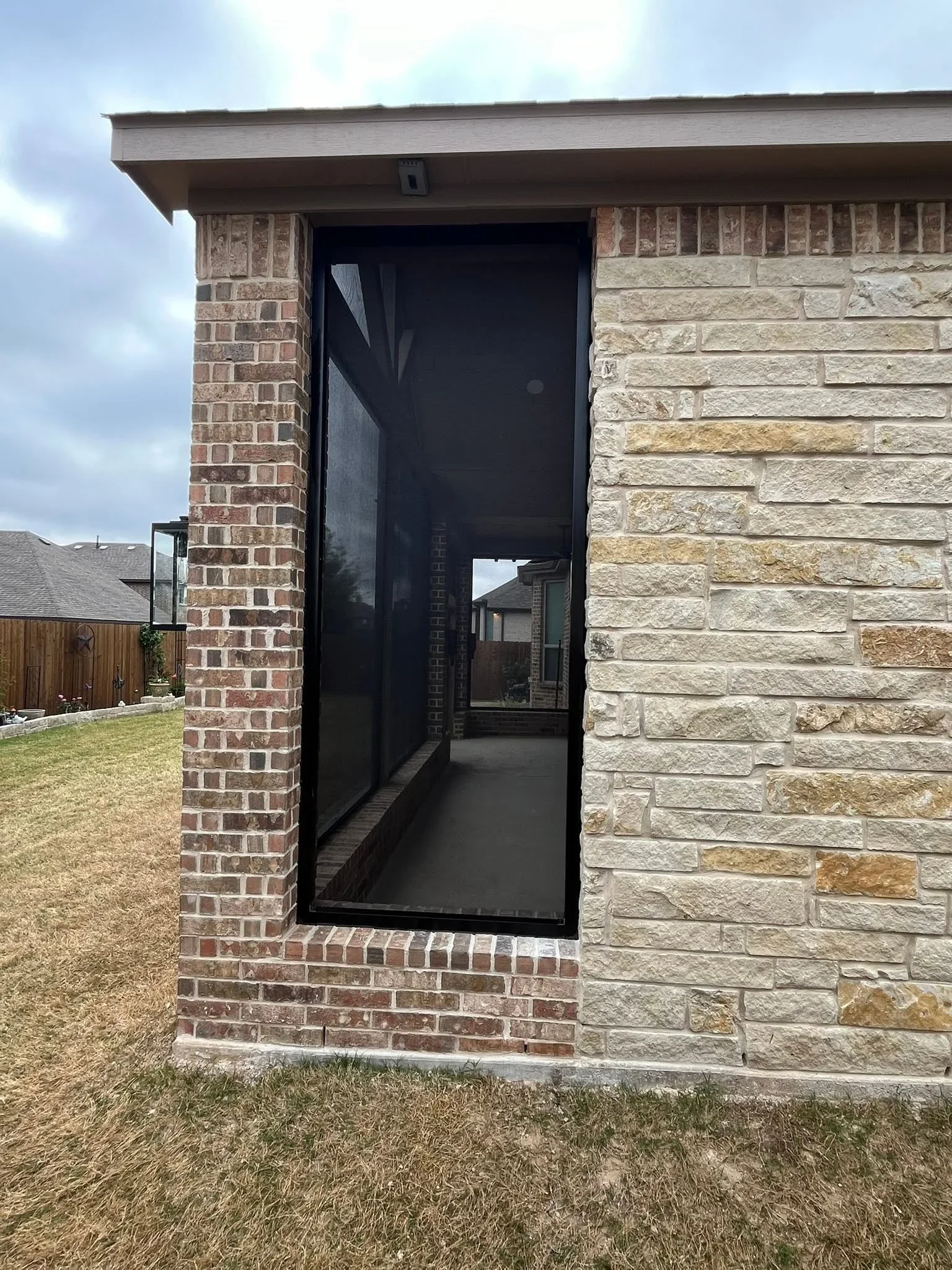 Black aluminum door frame installed between red brick and tan stone veneer exterior walls