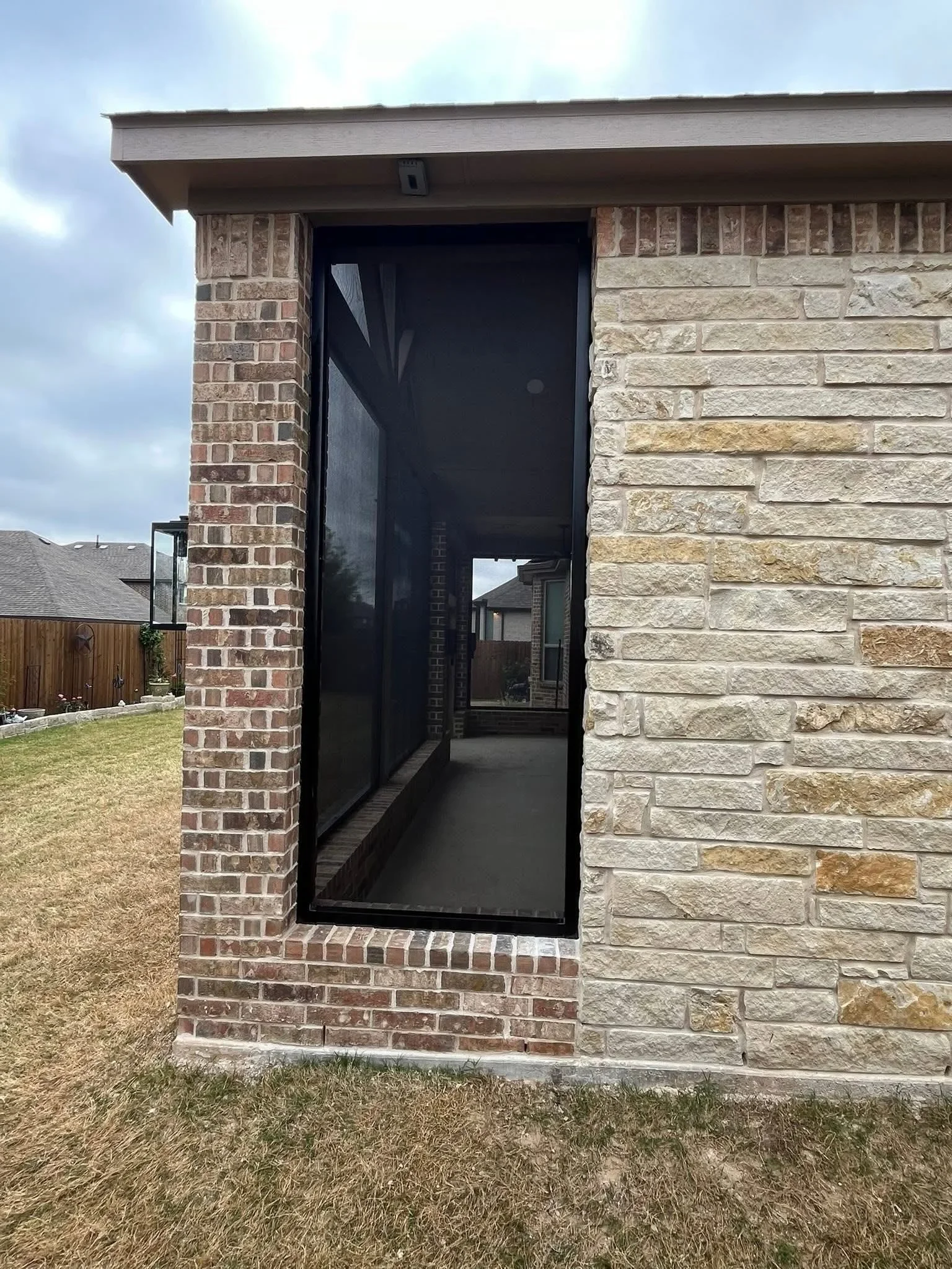 Black aluminum screen door between red brick and tan stone masonry walls