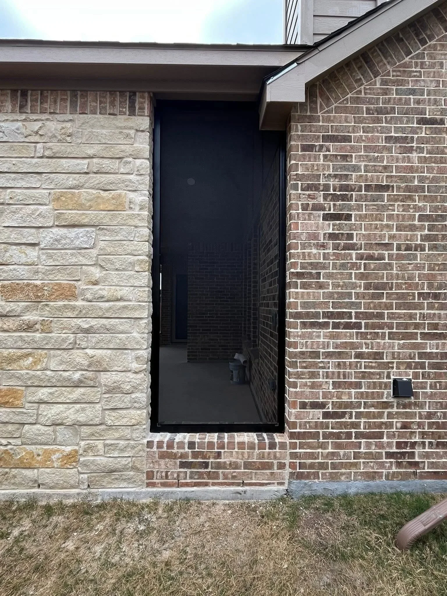 Black steel entry gate between stone and brick pillars at residential entrance