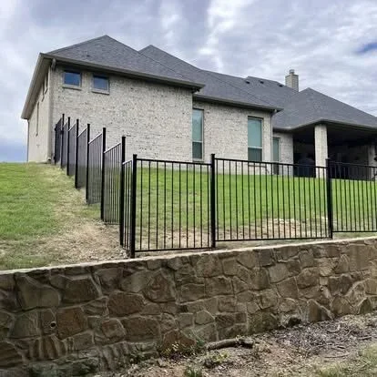 Black aluminum picket fence with vertical spindles installed along stone retaining wall at residential home