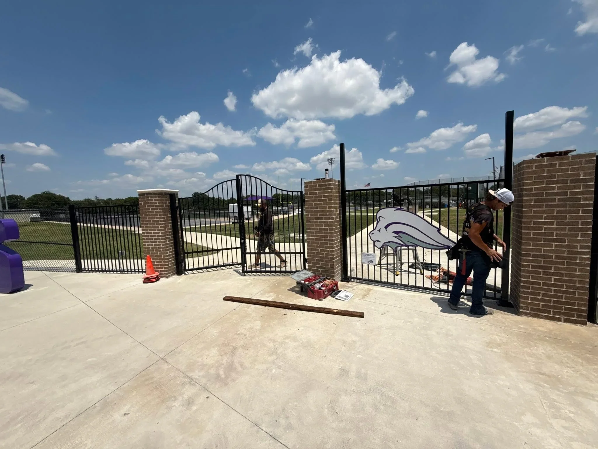 Black ornamental iron driveway gate with arched design between brick pillars at sports facility entrance