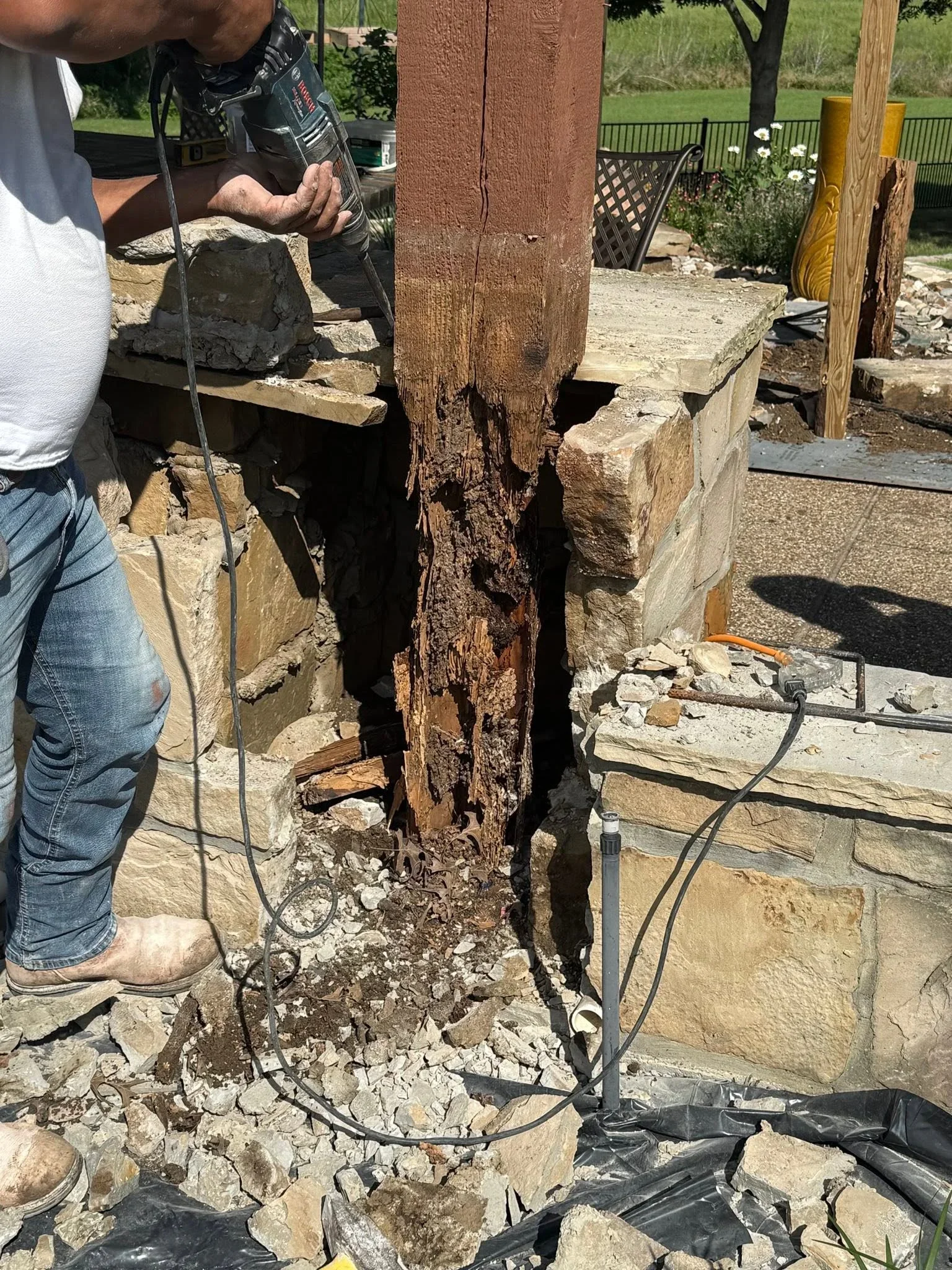 Rotted wooden fence post being removed with power tools, concrete foundation visible