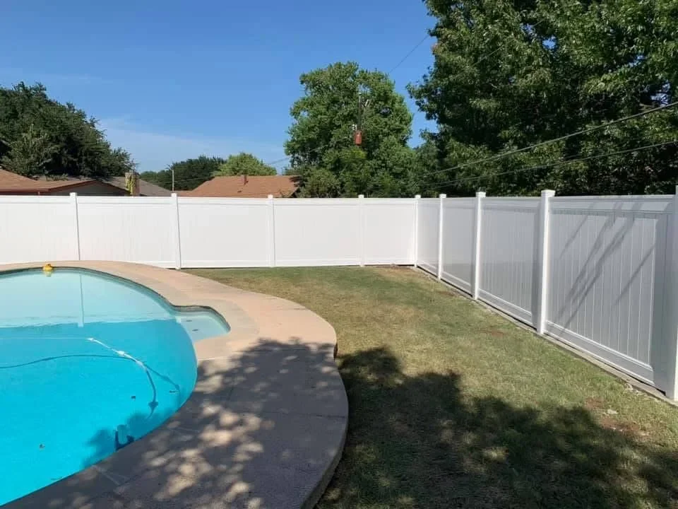 White vinyl privacy fence panels installed around in-ground pool with concrete deck