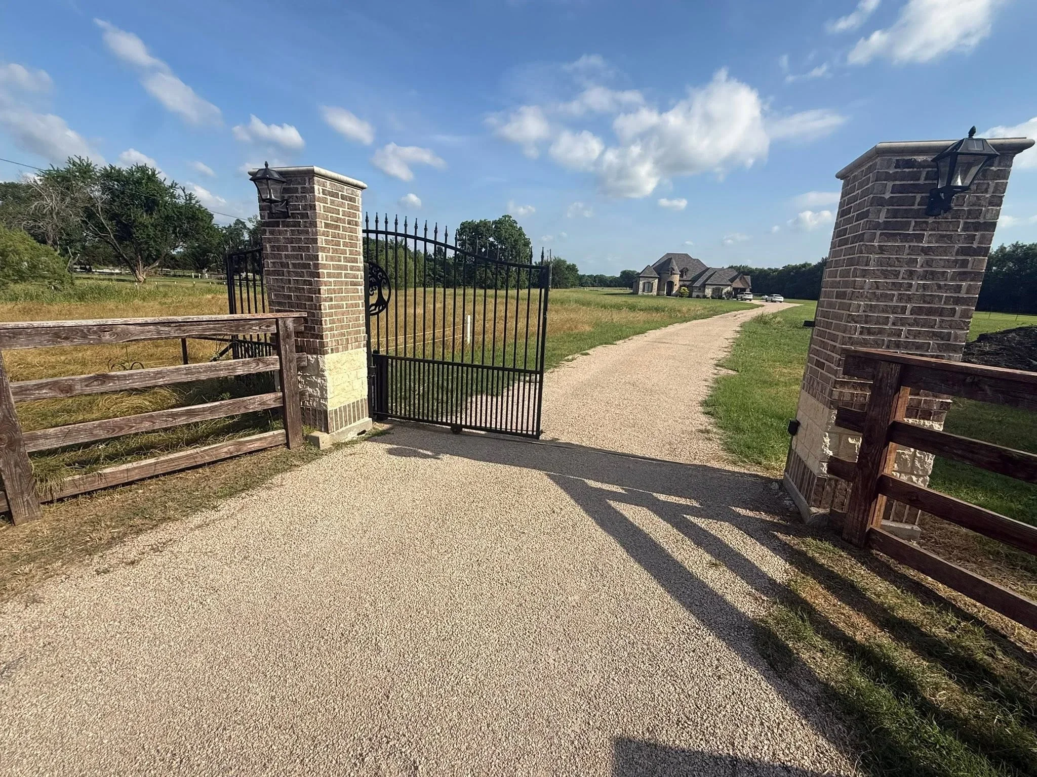 Black steel entry gate with brick pillars flanking gravel driveway